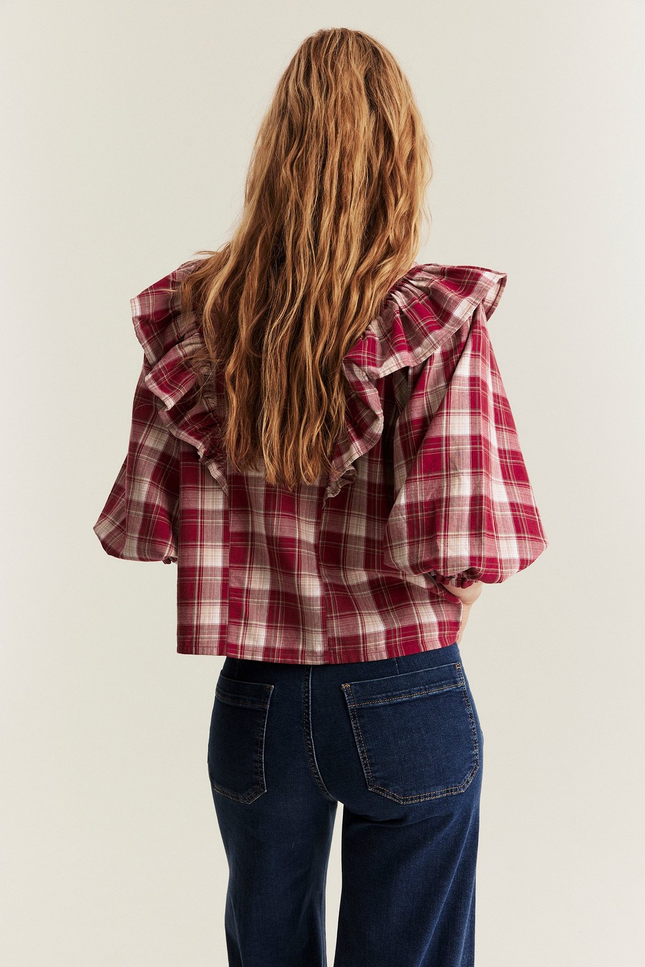 Ryggvy av kvinna i röd rutig bomullsblus med volanger och puffärmar, samt mörkblå jeans.