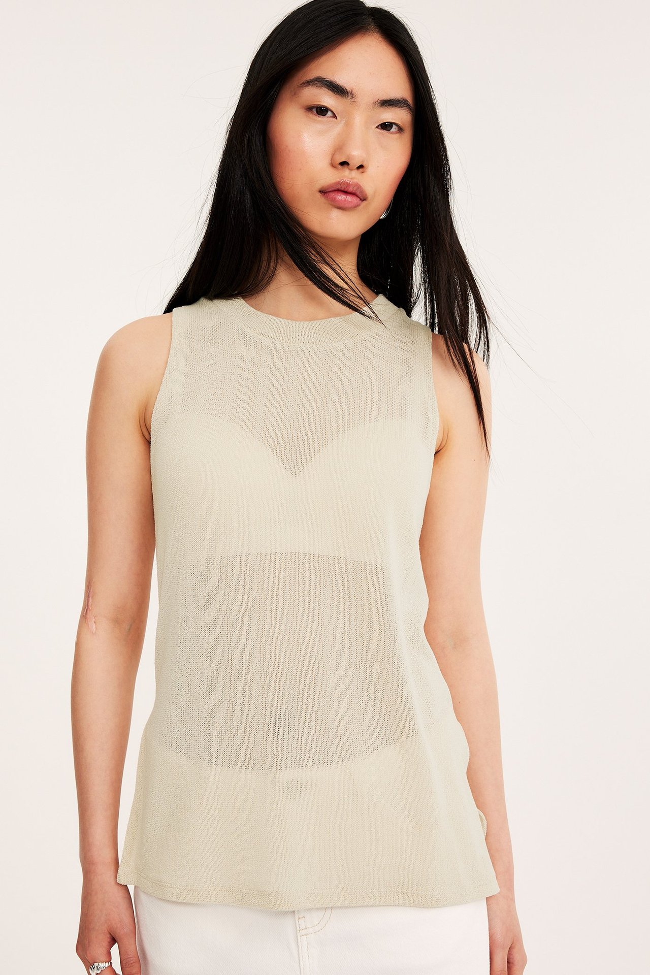 Forfra: kvinne i offwhite strukturert ermeløs topp over BH, med hvite bukser.