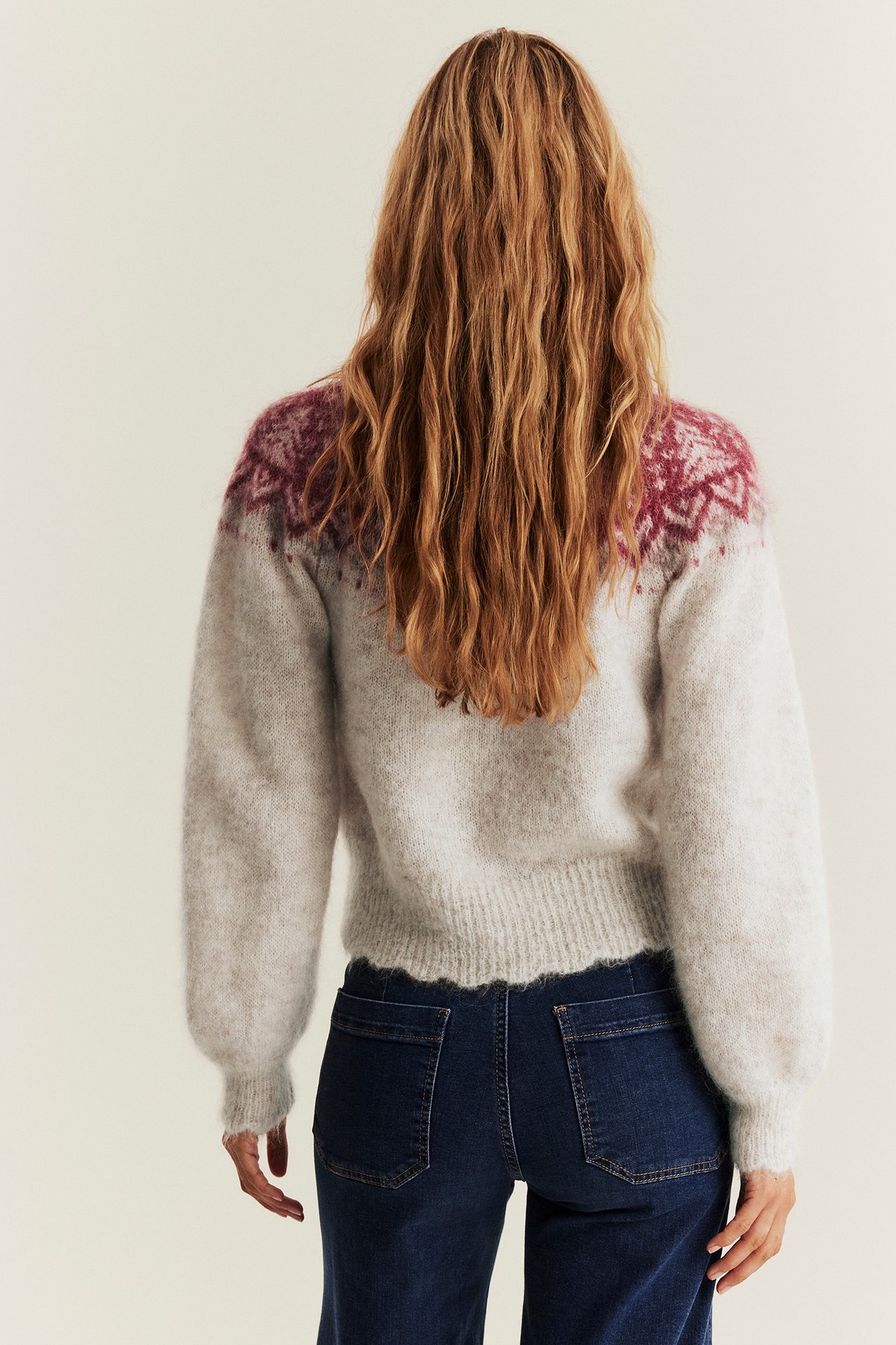 Bakfra på kvinne i beige melert jacquard-ullblandingskofte og mørkeblå jeans.