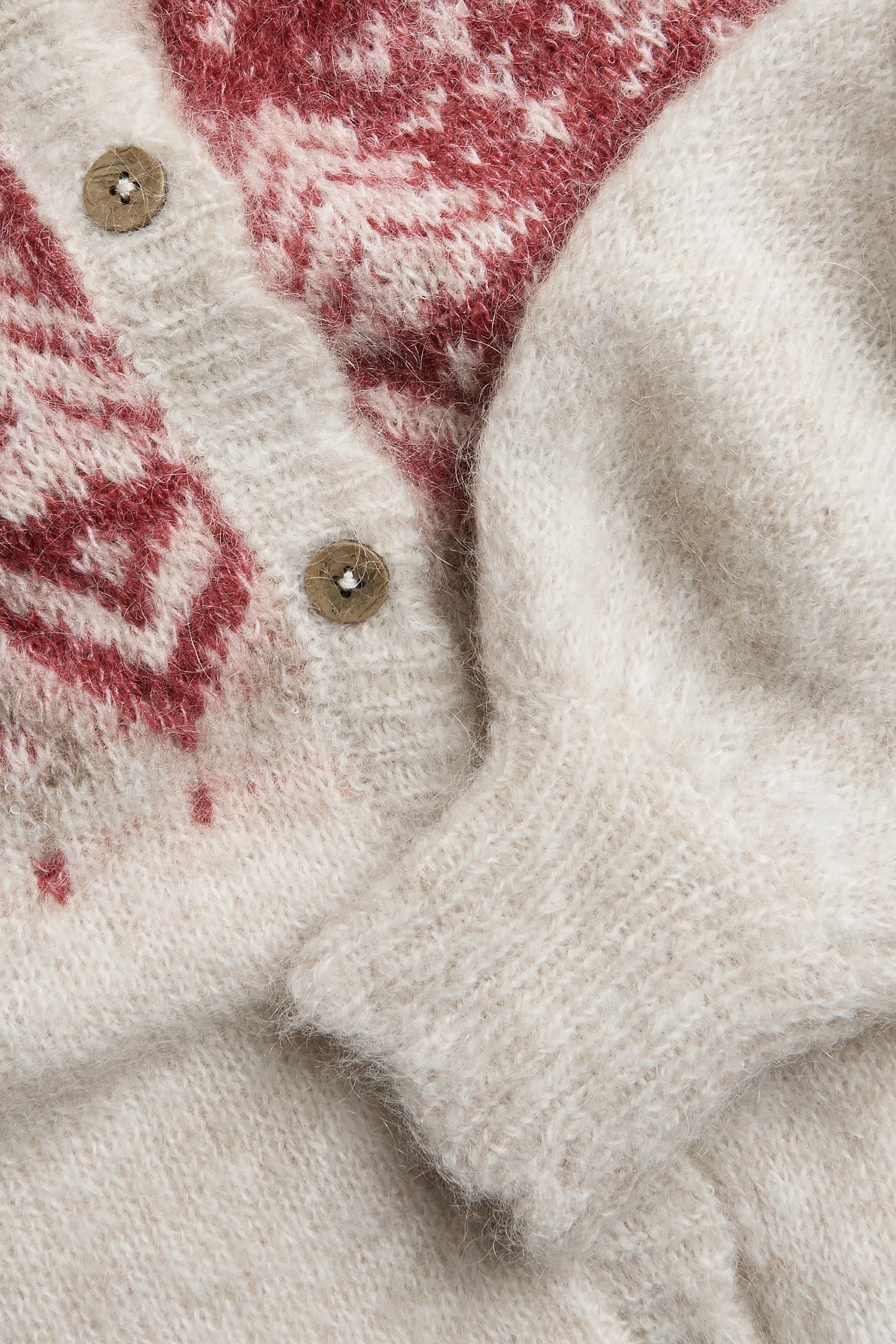 Nærbilde av en beige melange strikket cardigan med rødt jacquardmønster og brune knapper.