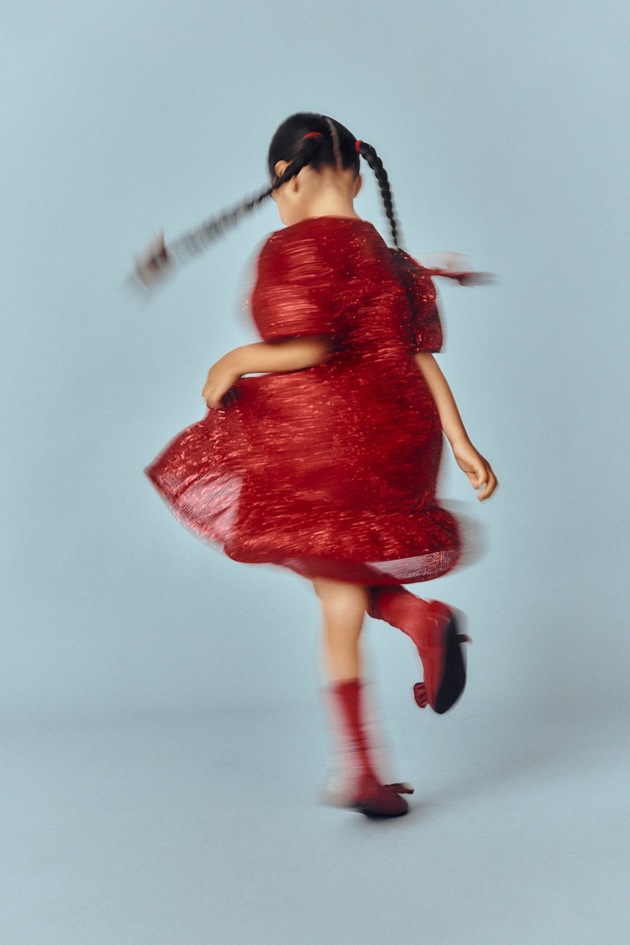 Widok z tyłu dziecka w czerwonej, brokatowej sukience z bufiastymi rękawami i czerwonych butach.