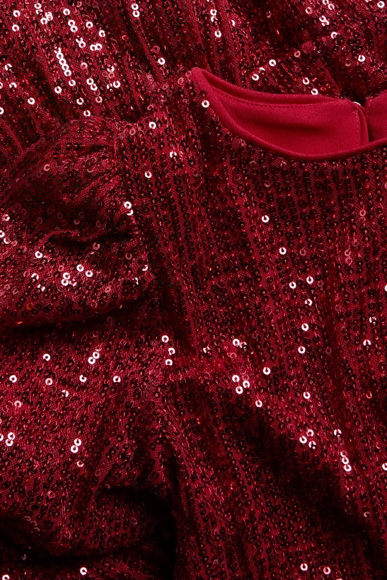 Zbliżenie czerwonej dziecięcej sukienki cekinowej z bufiastymi rękawami i guzikiem.