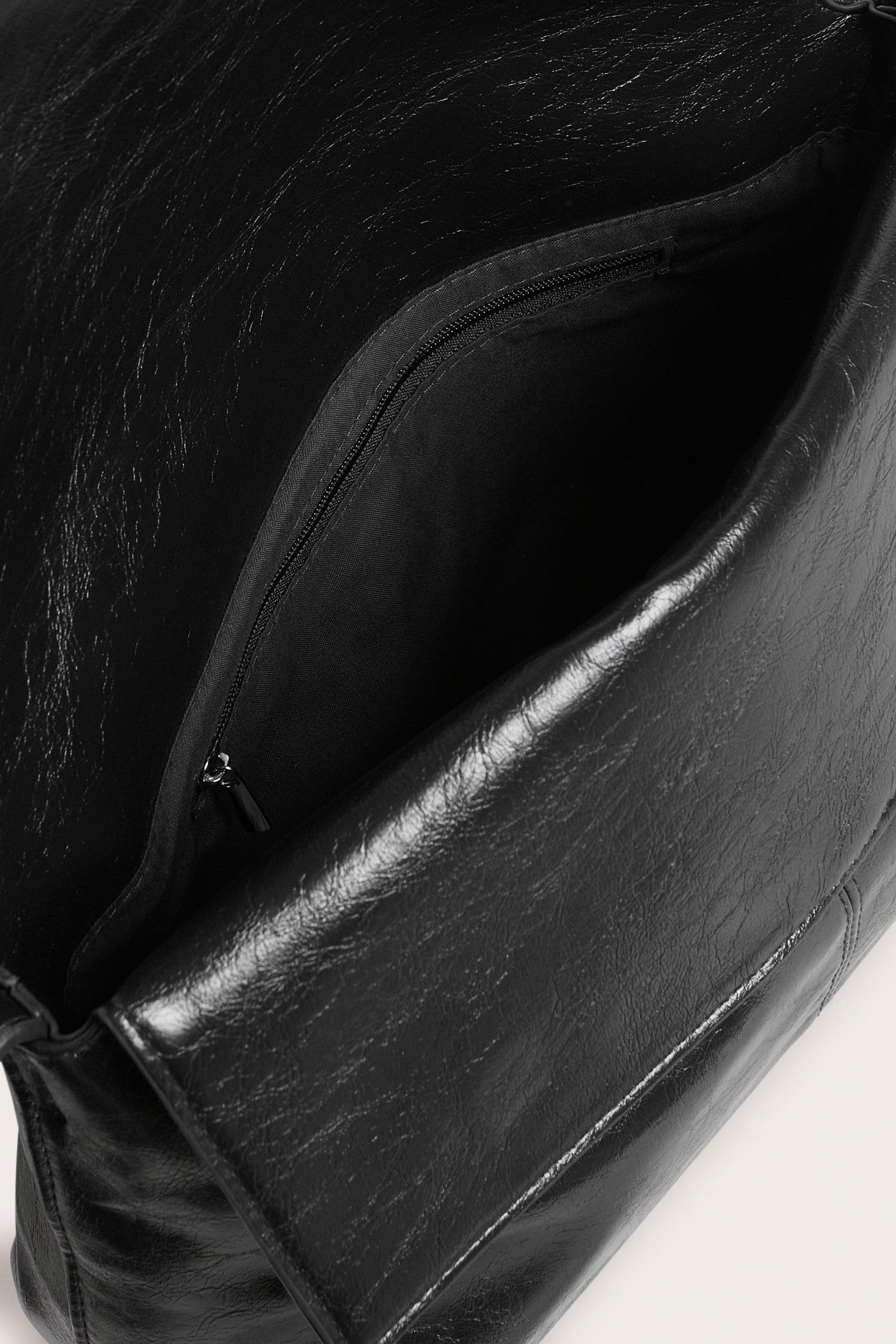 Lähikuva avoimesta mustasta olkalaukusta, jossa on halkeilevaa tekonahkaa ja vetoketjullinen sisätasku.