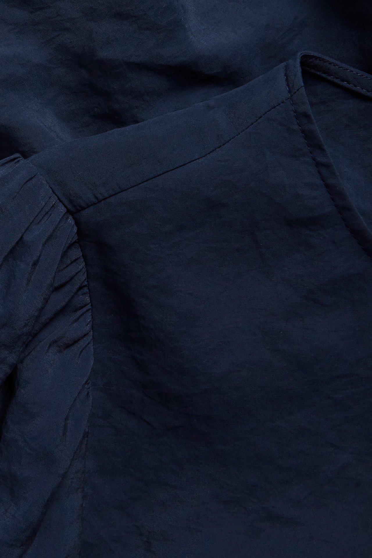 Zbliżenie na granatową, jednolitą bluzkę z wiązaniem z mieszanki modalu, z marszczonymi rękawami.