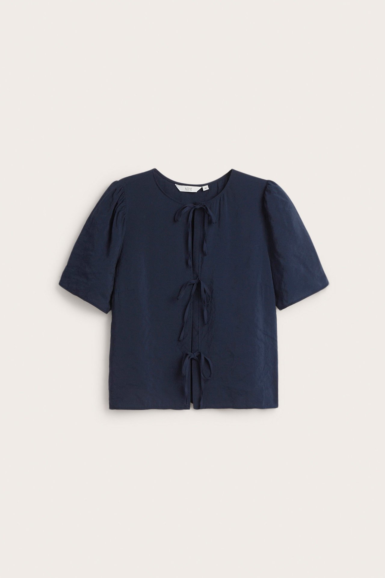 Widok z przodu granatowej, jednolitej bluzki z krótkim rękawem, okrągłym dekoltem i wiązaniami z przodu.