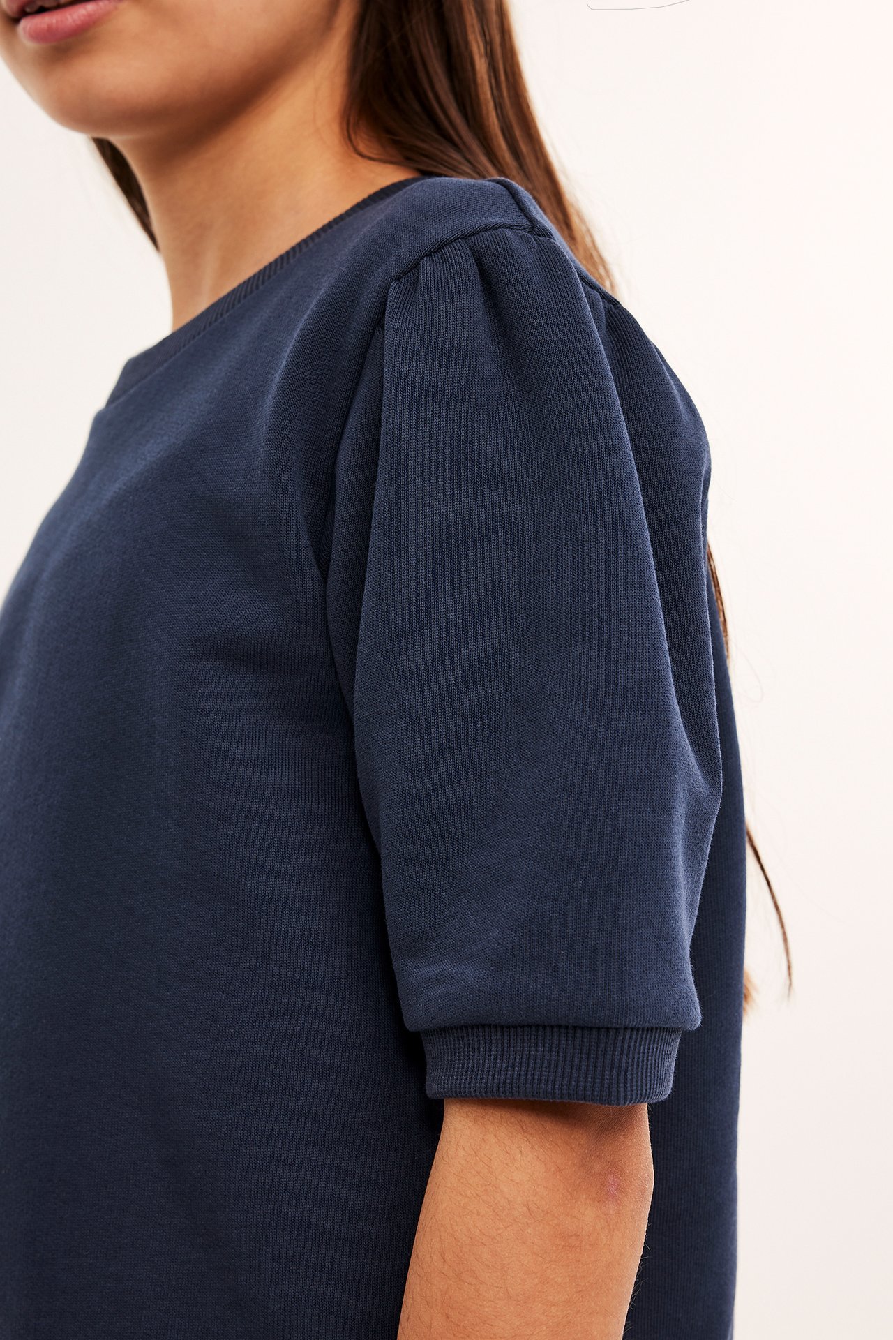 Närbild, sidovy av ett barn i en marinblå kortärmad sweatshirt med puffärm och rund hals.