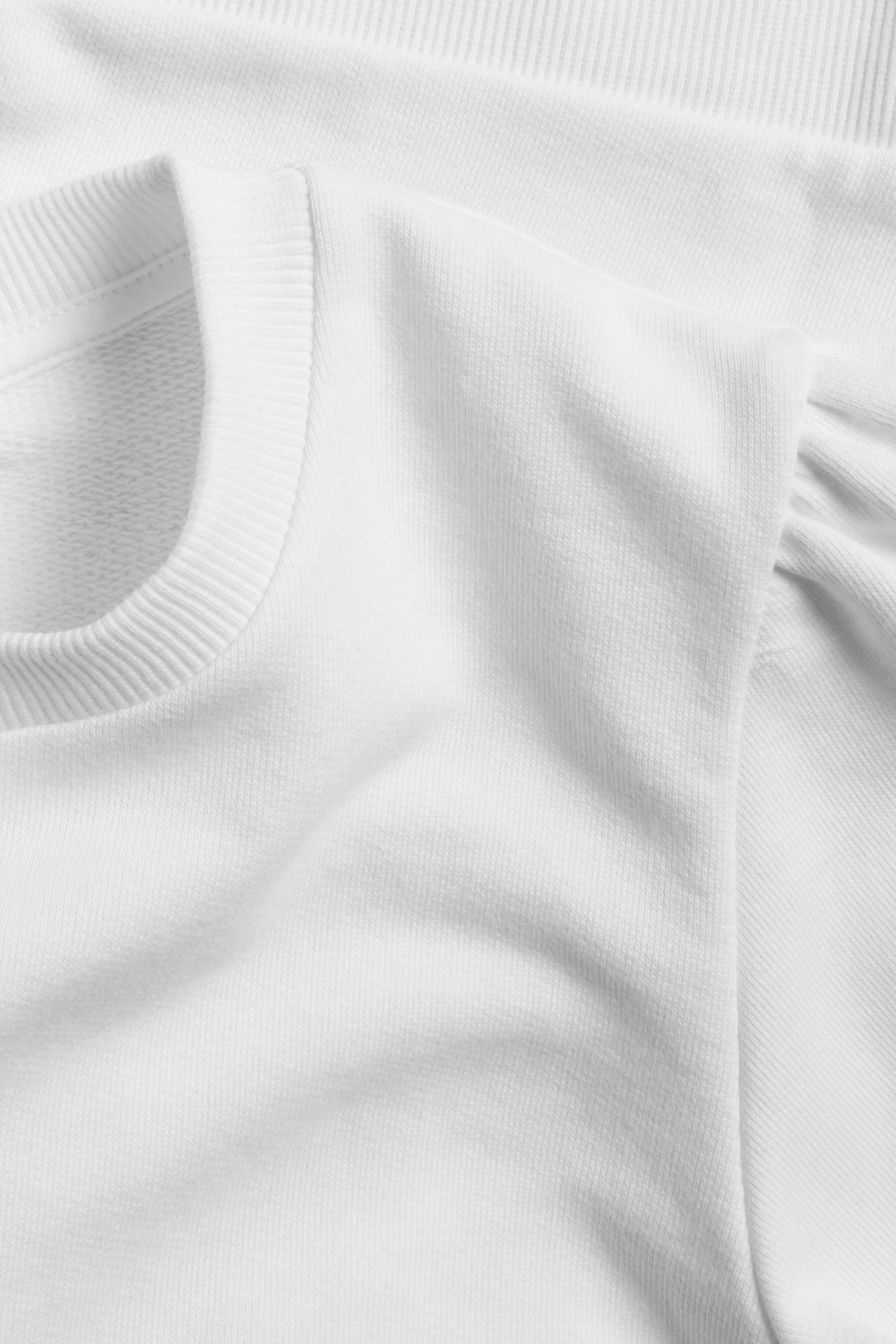 Zbliżenie białej bawełnianej bluzy z krótkim rękawem, bufiastymi rękawami i prążkowanym dekoltem.