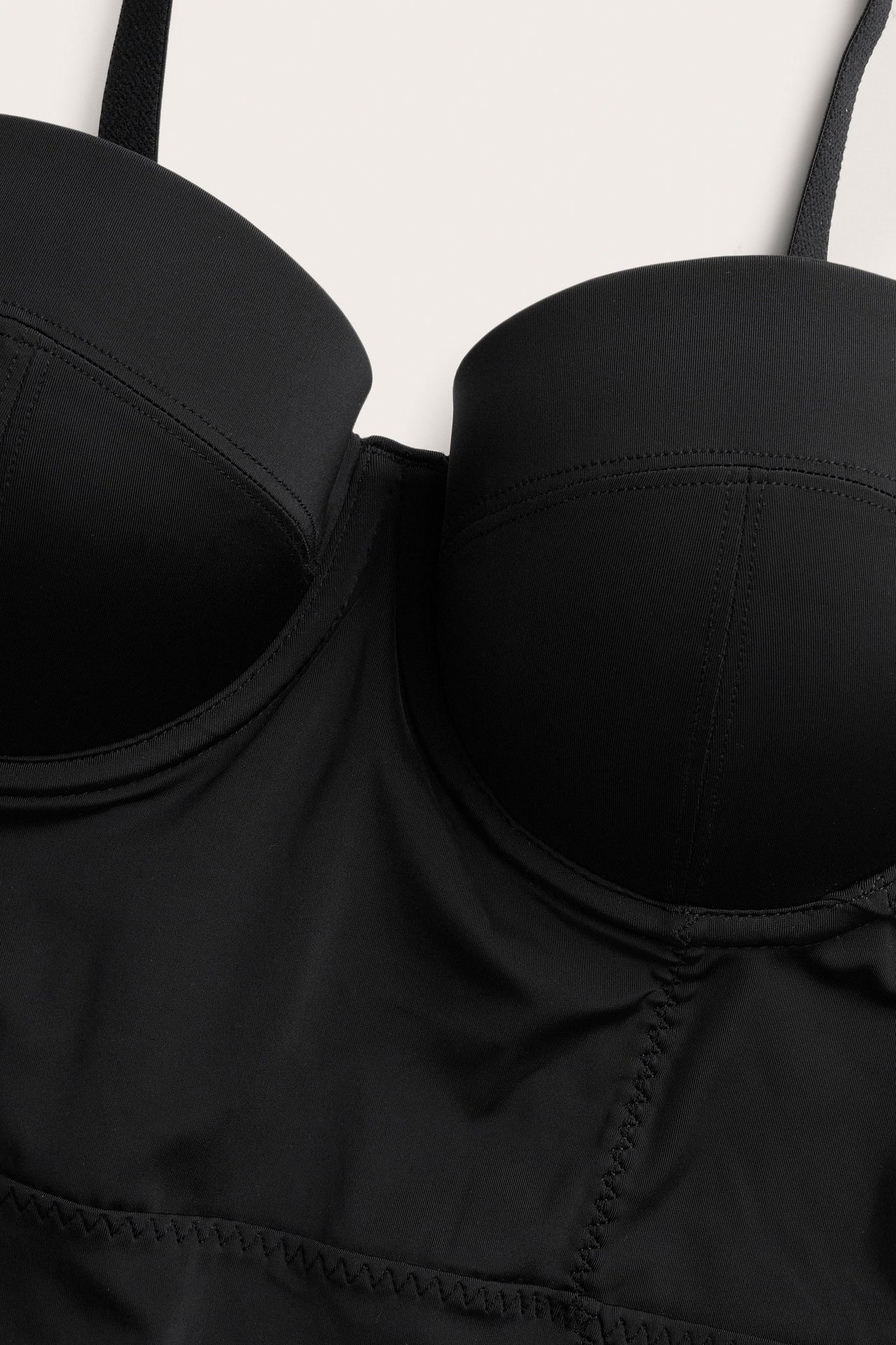 Nærbilde av en svart formende body med formstøpte cuper, detaljerte sømmer og justerbar stropp.