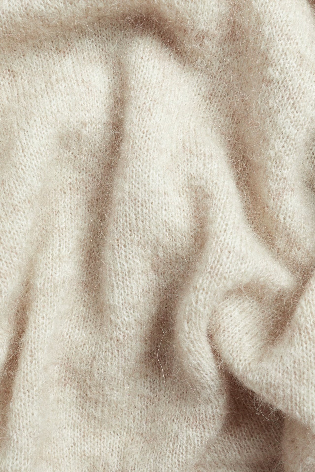 Zbliżenie beżowego melanżowego dzianinowego materiału z mieszanki moheru o miękkiej, puszystej fakturze.