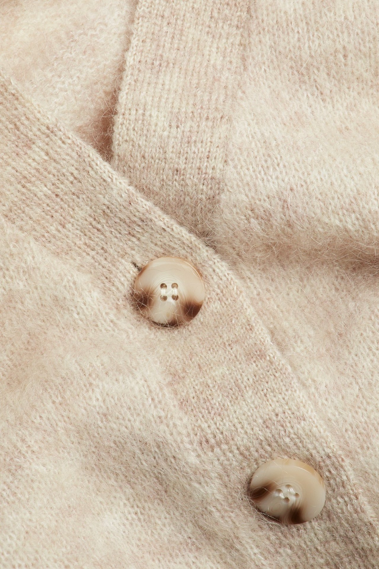 Zbliżenie beżowego kardiganu z mieszanki moheru z dwoma marmurkowymi brązowymi guzikami.