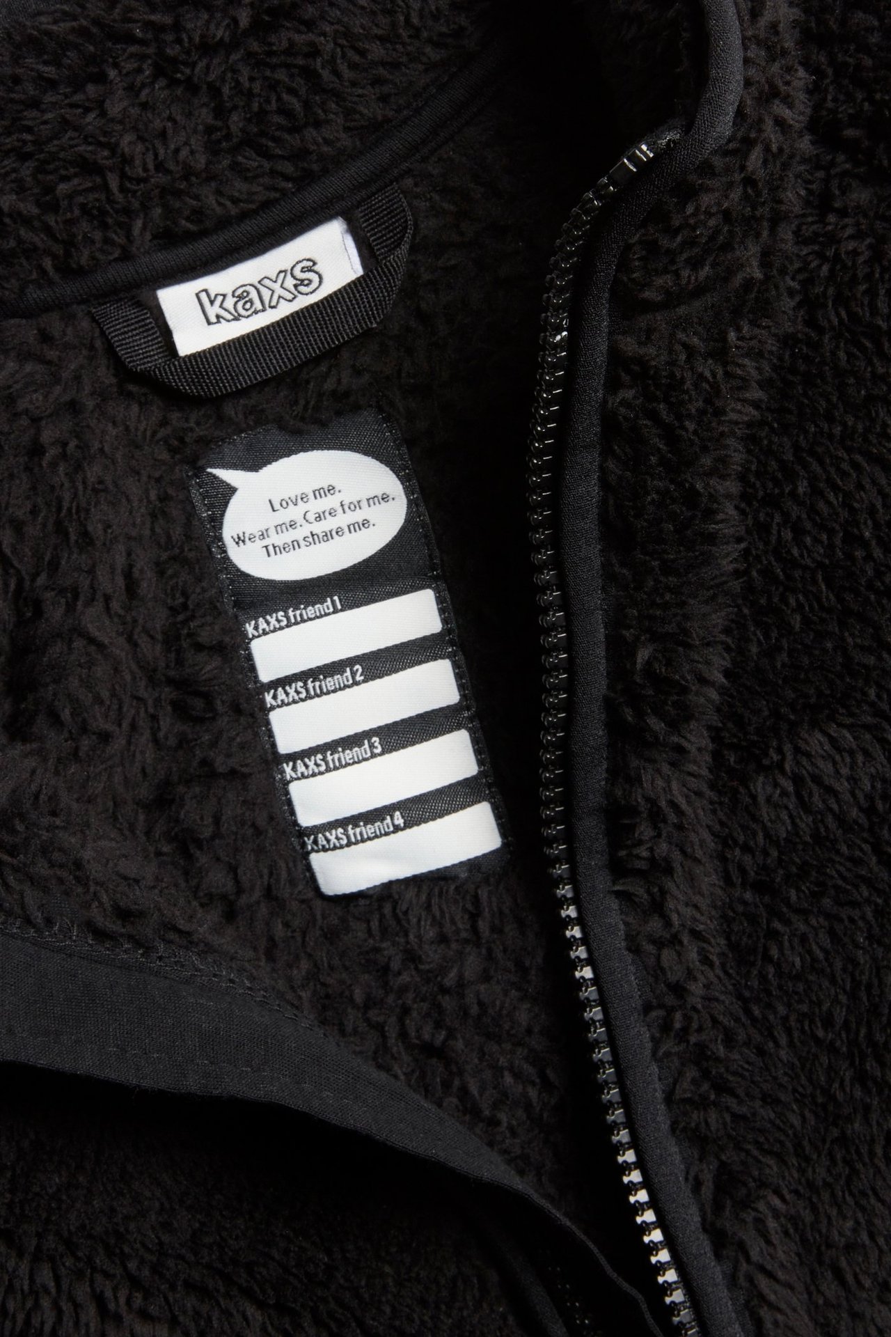 Zbliżenie czarnej kurtki polarowej z zamkiem błyskawicznym, metką marki i białą wszywką na imię.