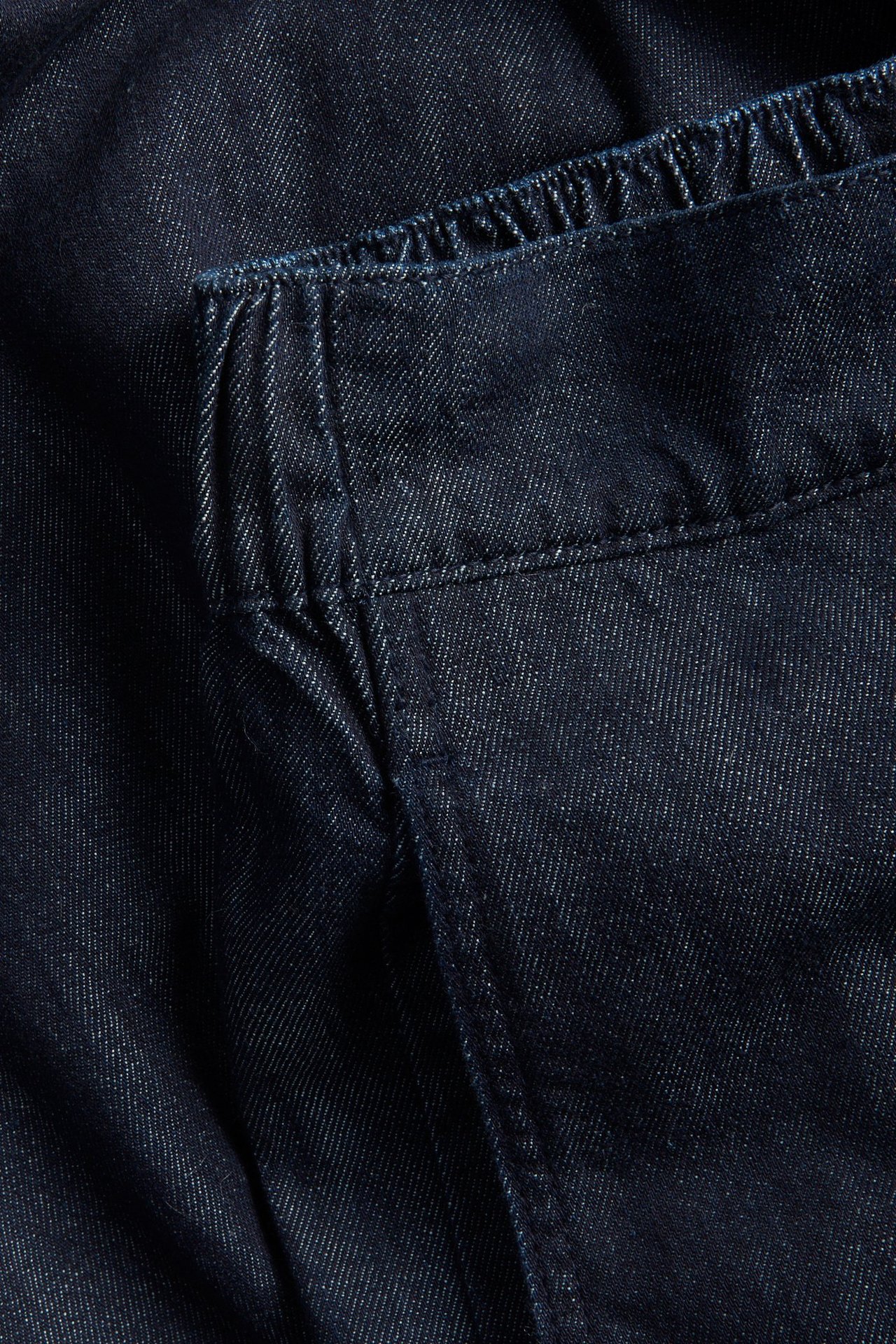 Zbliżenie na ciemne bawełniane jeansy z elastycznym pasem i widocznymi szwami.