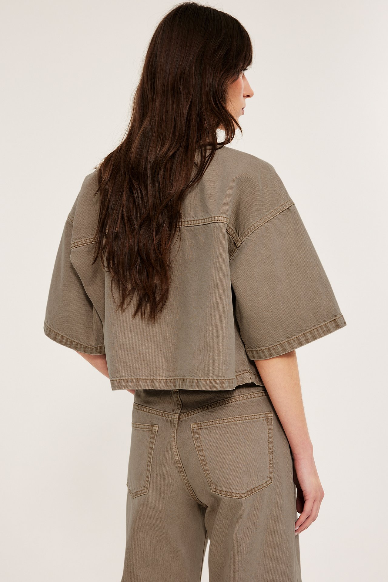 Ryggvisning av en kvinne i en løstsittende, kort brun twillskjorte og matchende brune bukser.