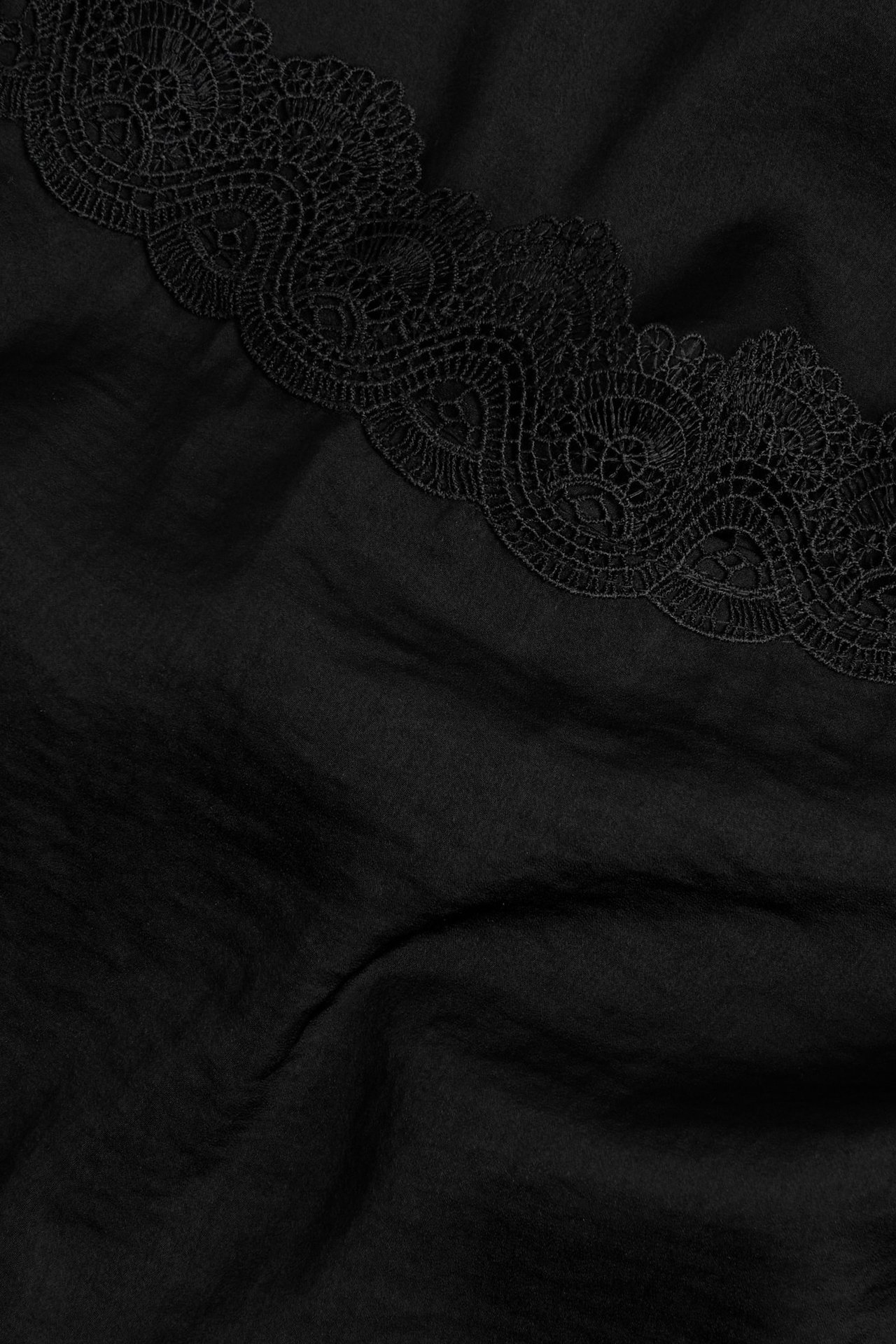 Zbliżenie czarnej satynowej koszulki z misterną czarną koronką.