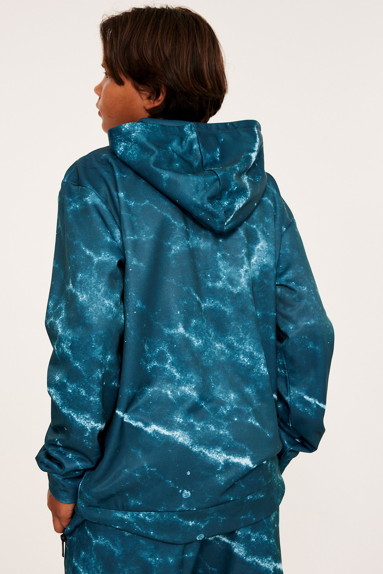 Bakifrån, ett barn i en grön mönstrad polyesterhoodie och matchande byxor.