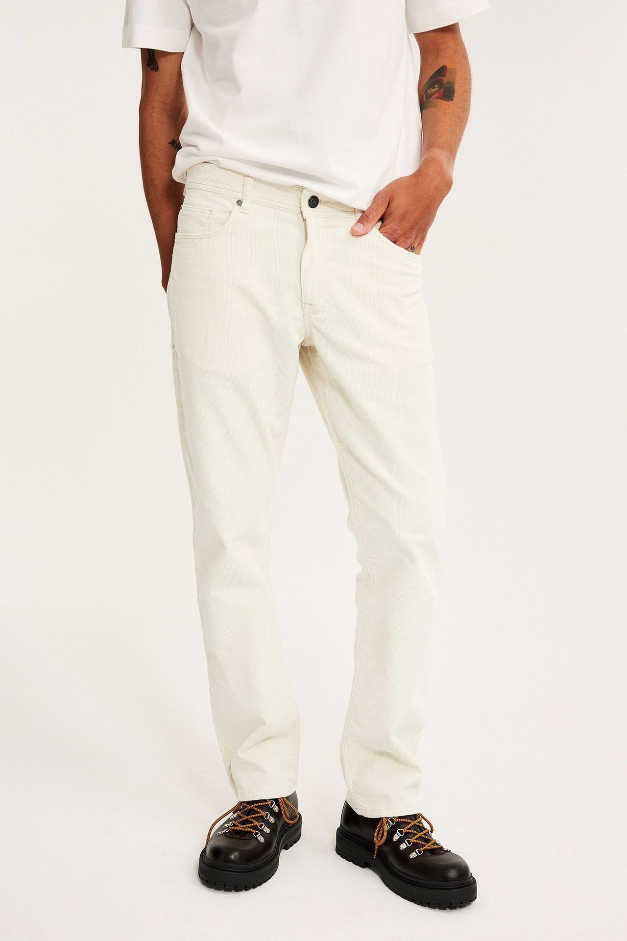 Frontvy av man i offwhite manchesterbyxor, vit t-shirt och mörkbruna snörskor.