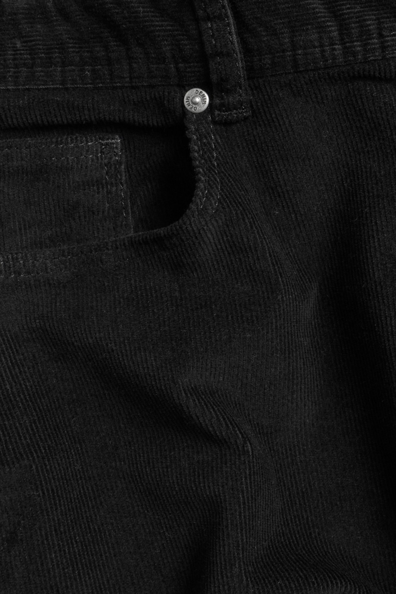 Zbliżenie czarnych sztruksowych spodni, przedstawiające przednią kieszeń i srebrny guzik.