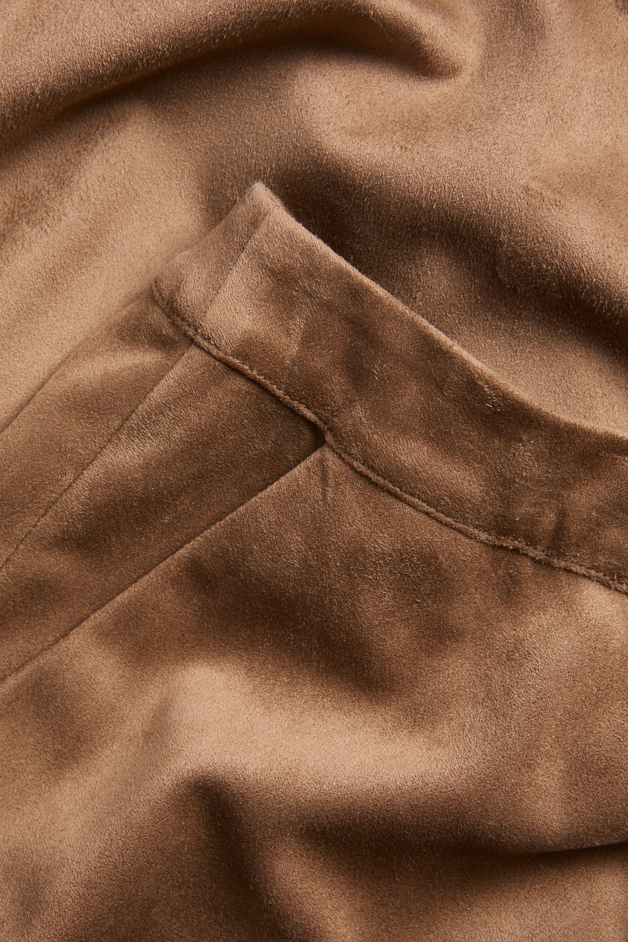 Zbliżenie na brązowy materiał spódnicy z imitacji zamszu, ukazujące jego miękką fakturę i szew.