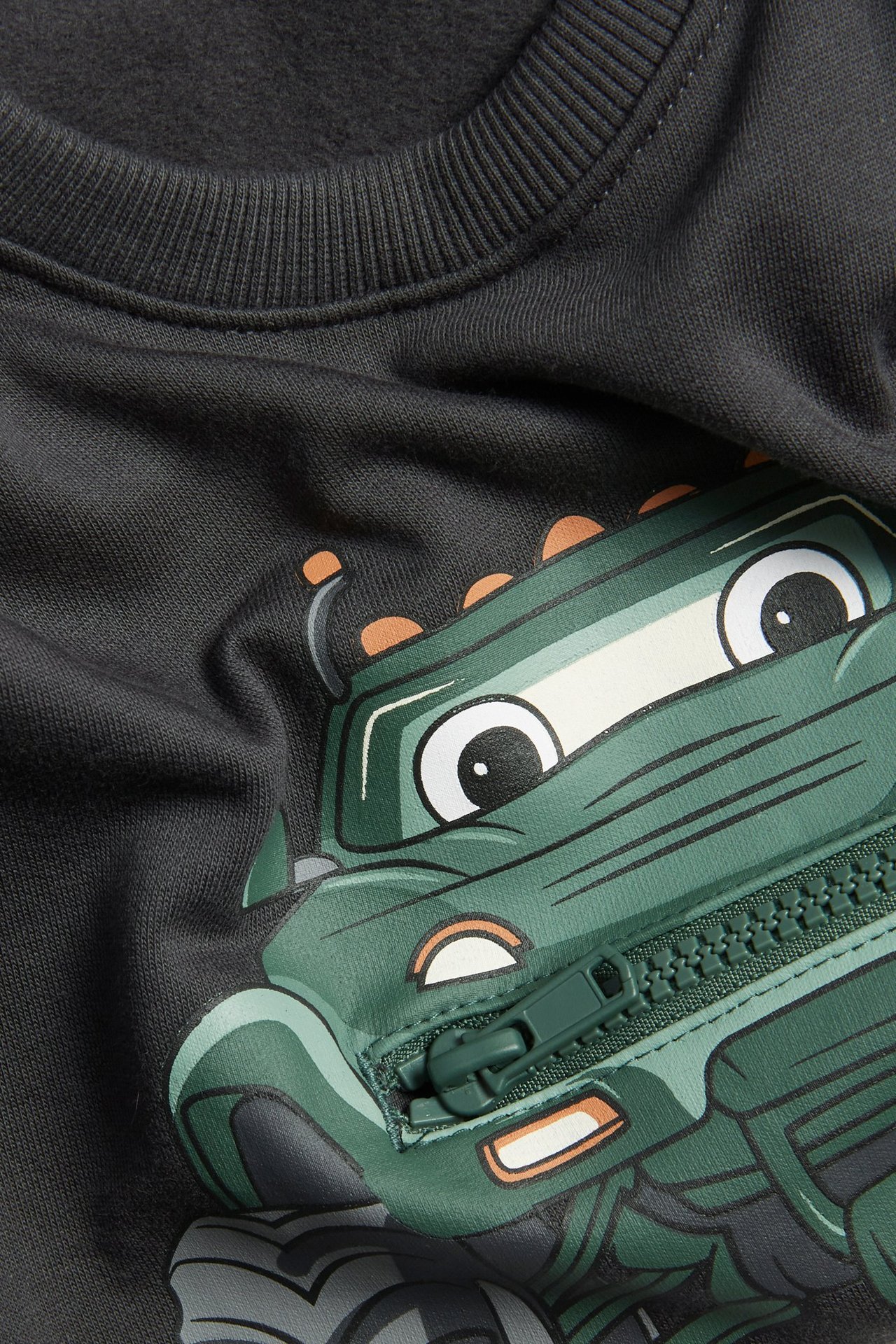 Zbliżenie czarnej bawełnianej bluzy dziecięcej z zielonym nadrukiem monster trucka i zamkiem błyskawicznym.