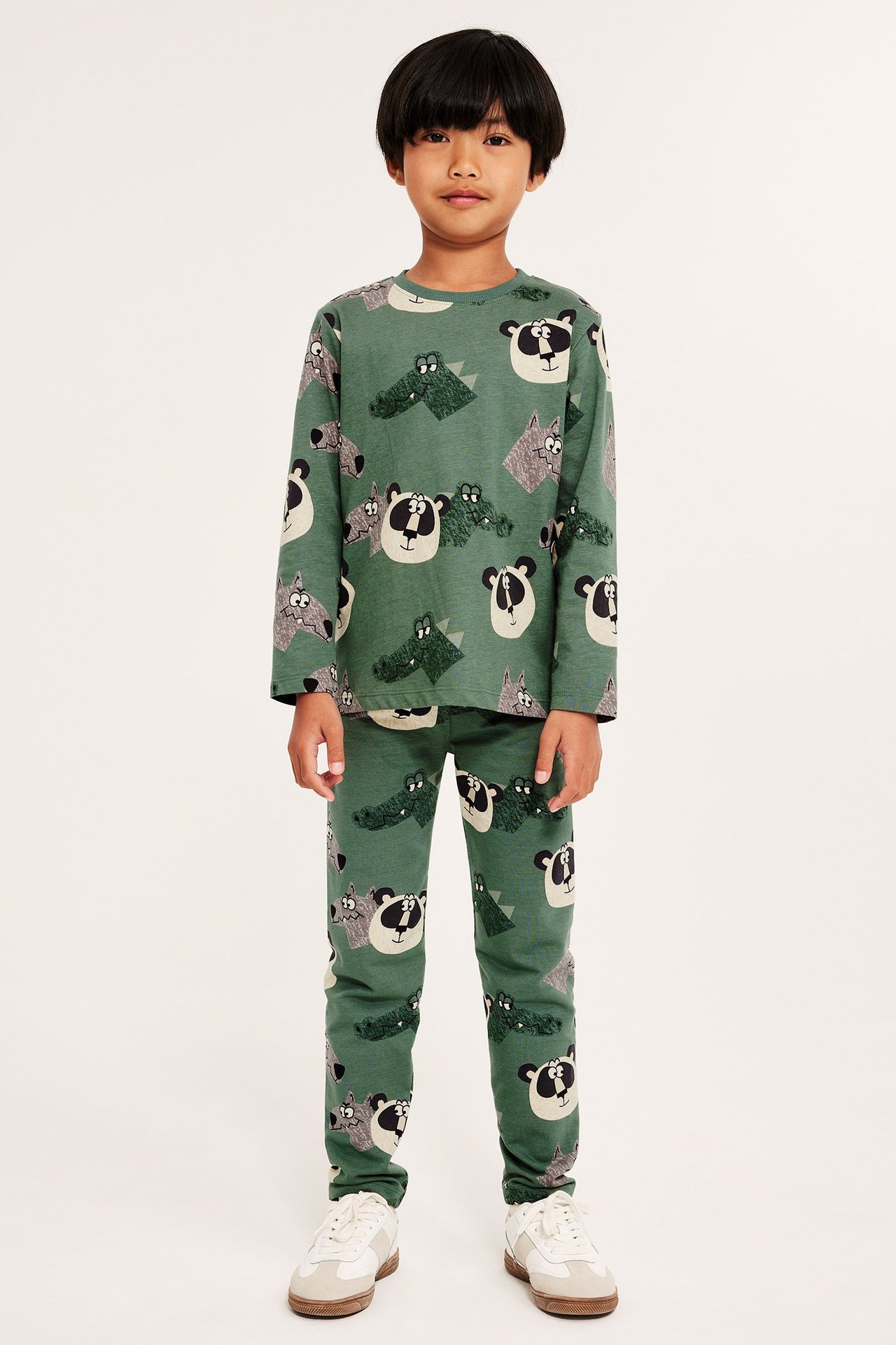 Edestä: Lapsi tummanvihreässä eläinkuvioisessa pitkähihaisessa puuvillapaidassa, leggingseissä ja lenkkareissa.