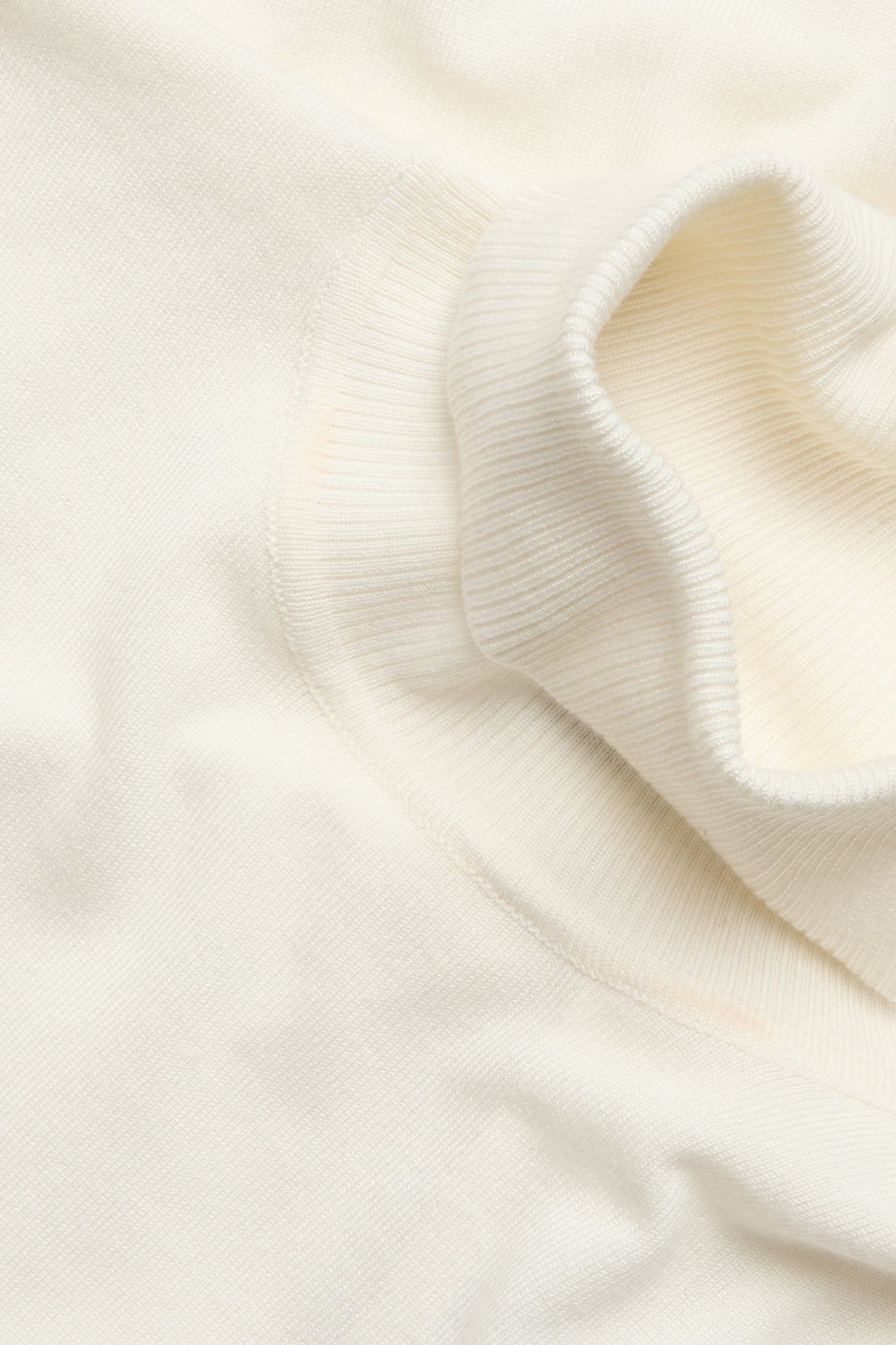 Zbliżenie na kremowy, drobno dziany golf, ukazujące miękki materiał i prążkowany mankiet.