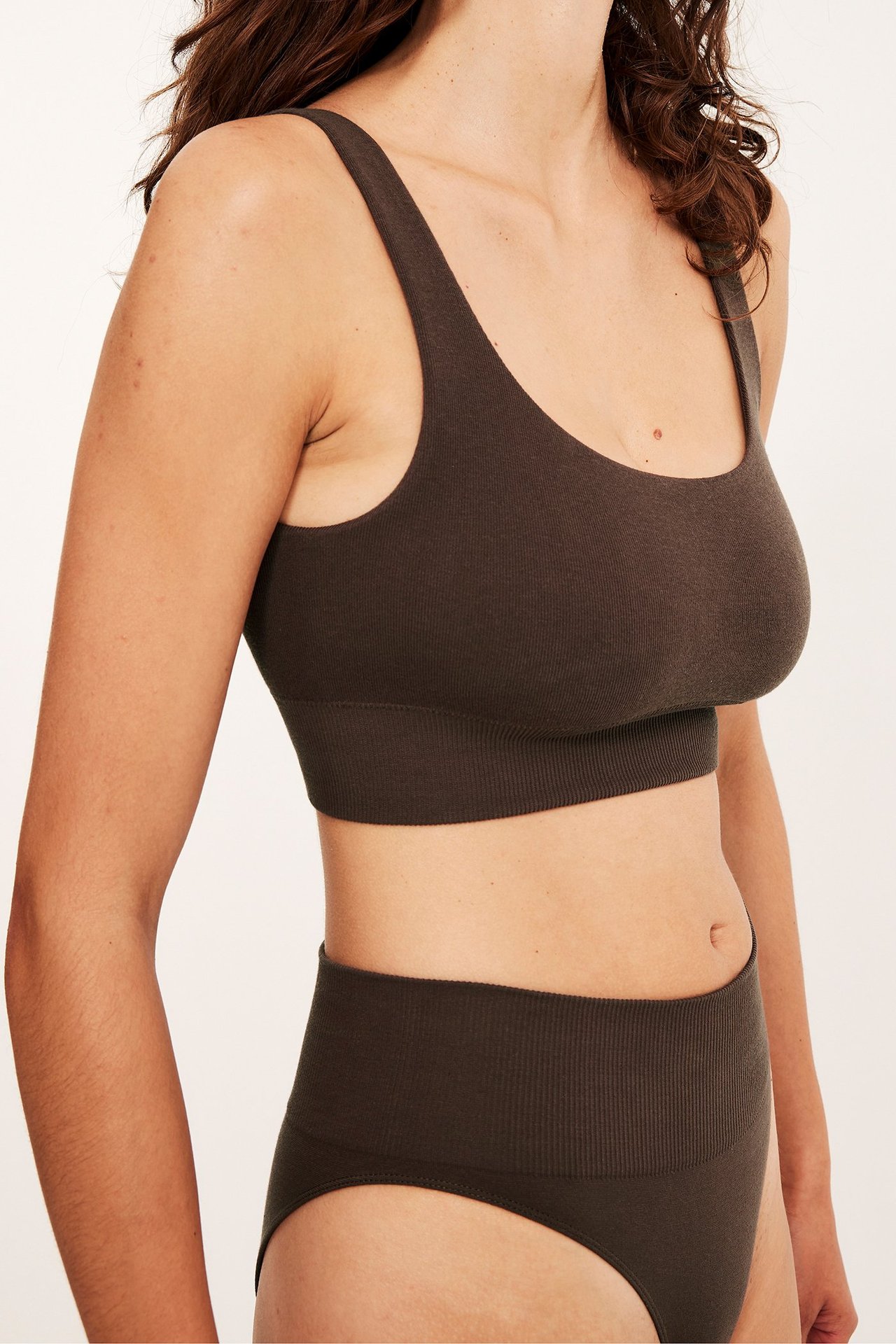 Närbild framifrån-sidan på en kvinna som bär en mörkbrun bh-topp i bomullsmix och matchande högmidjade trosor.