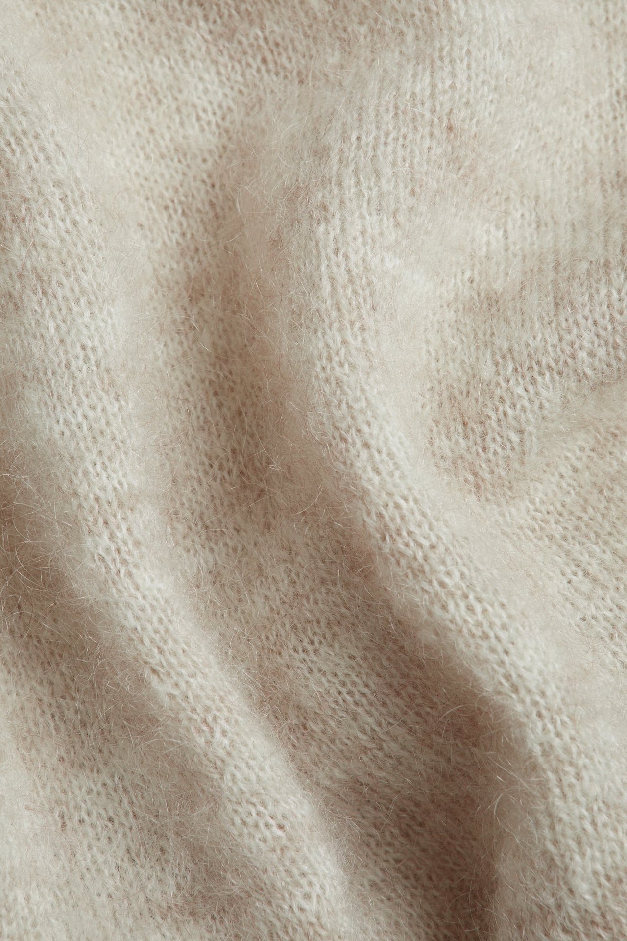 Zbliżenie beżowego melanżowego dzianinowego materiału z mieszanki moheru, ukazujące jego miękką teksturę.