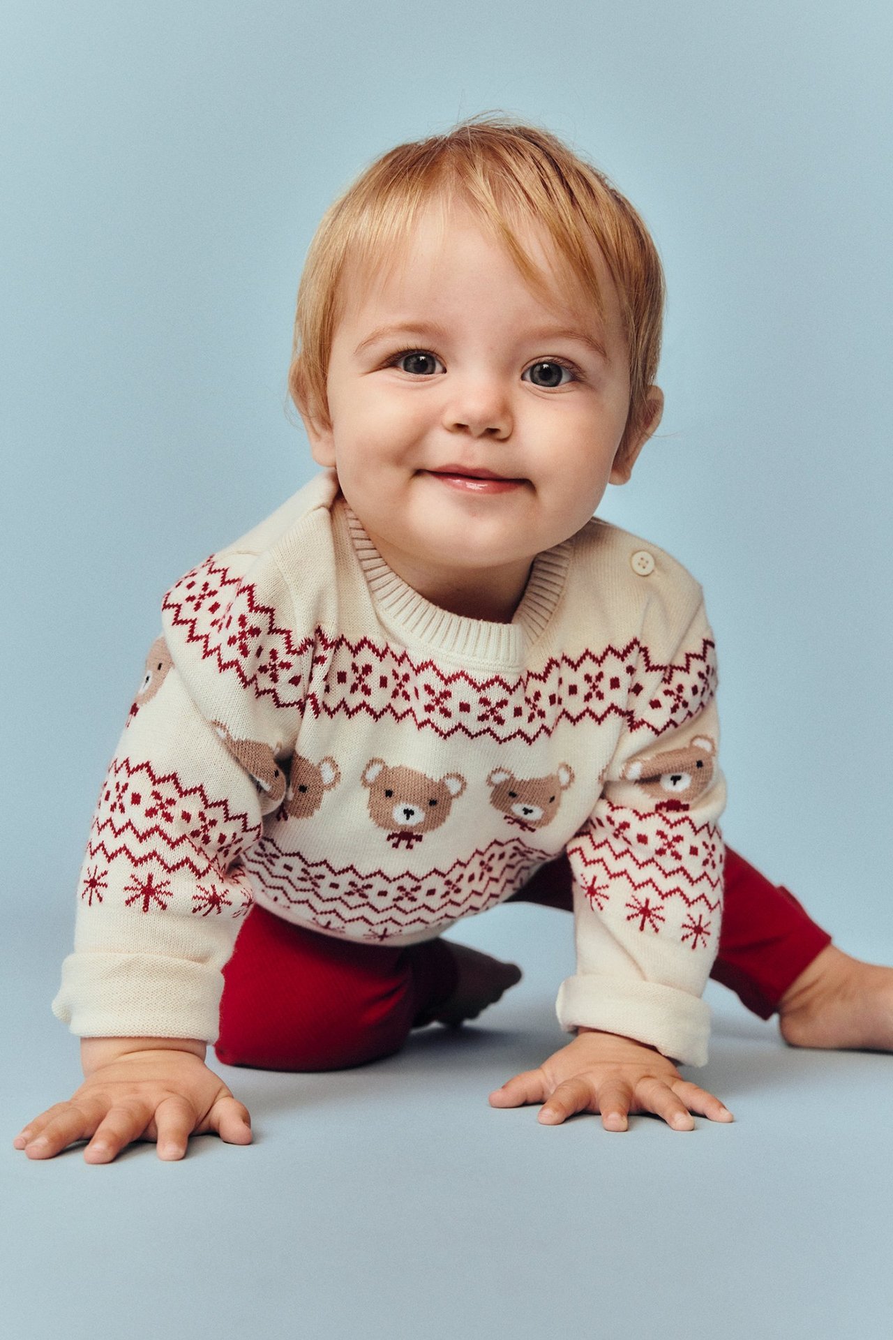 Etunäkymä: vauva yllään vaalea beige neulepusero punaisella jakardikuviolla, karhuilla ja punaisilla leggingseillä.