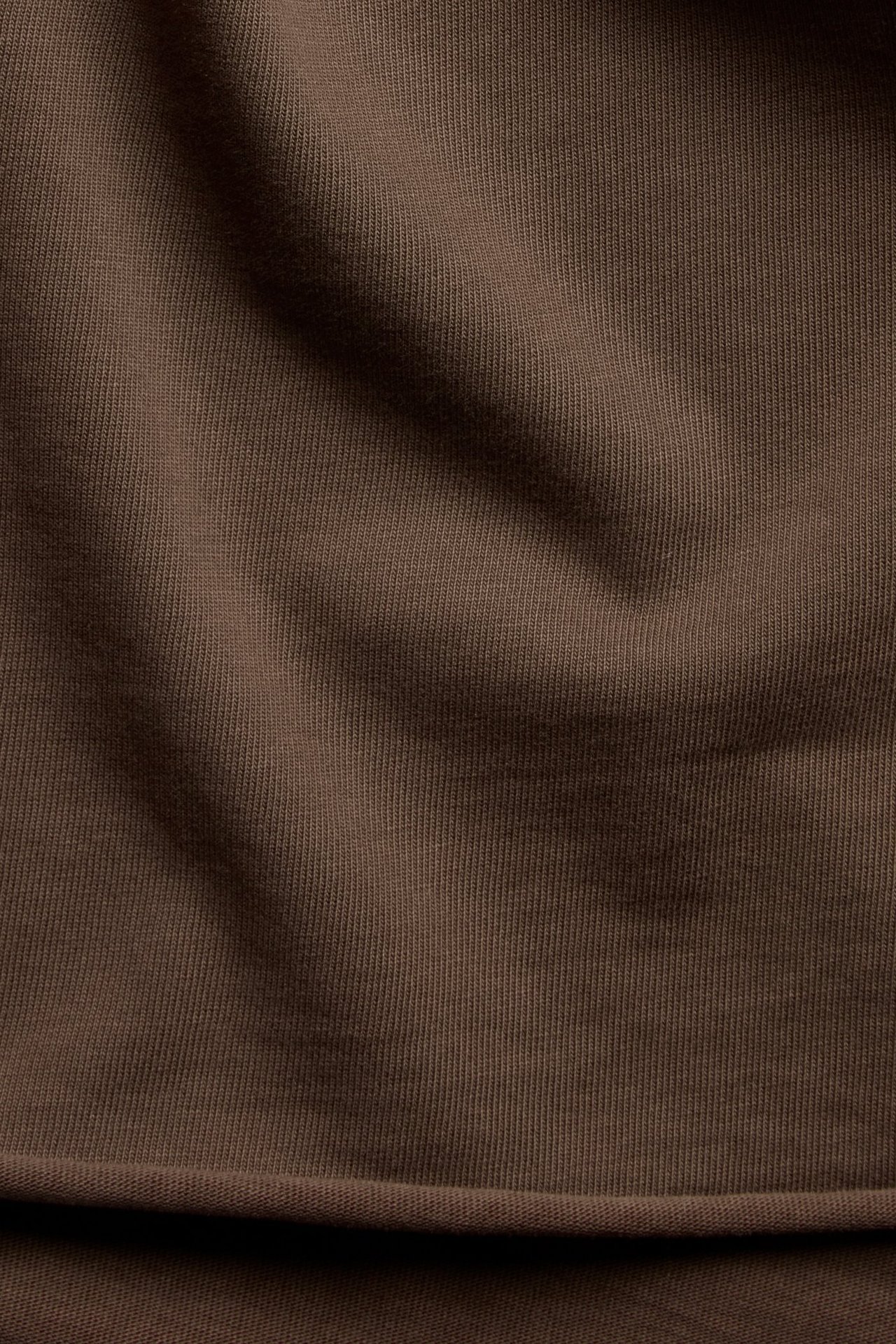 Zbliżenie na ciemnobrązowy prążkowany materiał bawełniany z surowym brzegiem i delikatnymi fałdami.