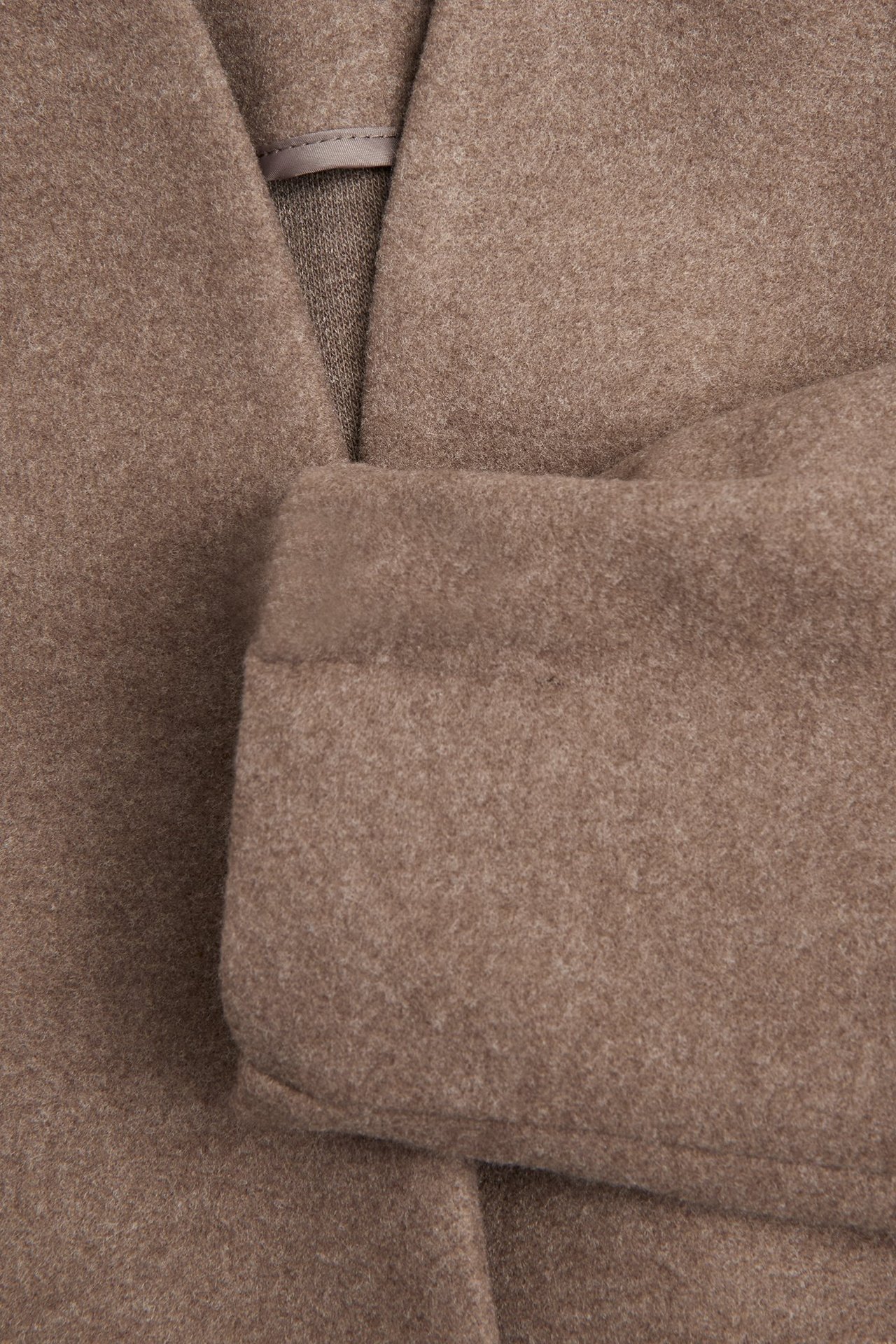 Zbliżenie brązowej wełnianej kurtki z otwartym dekoltem w serek i podwiniętym mankietem.