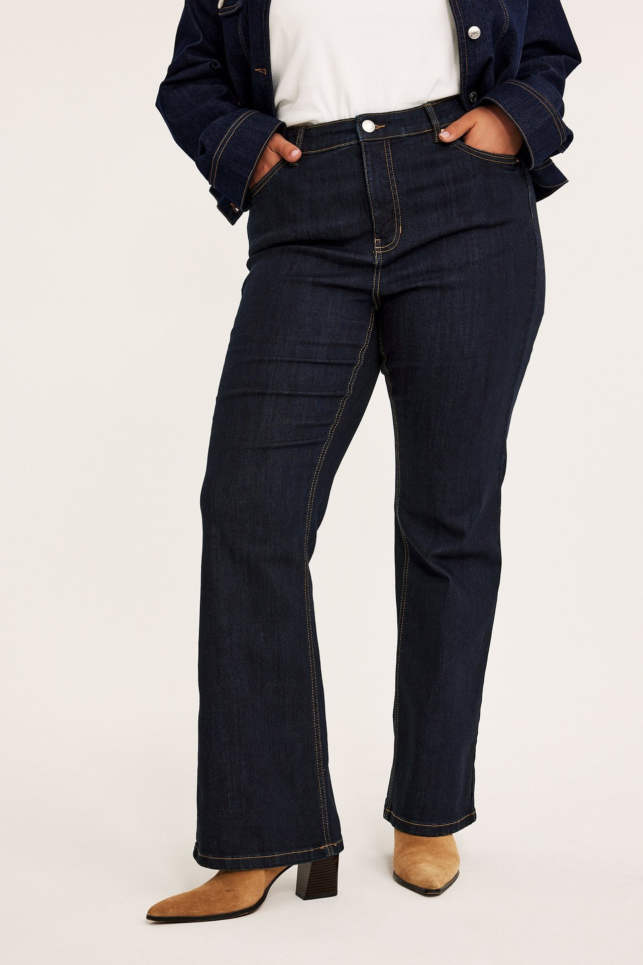 Framifrån: kvinna i mörkblå bootcut jeans med hög midja, vit t-shirt, jeansjacka och beiga ankelboots.