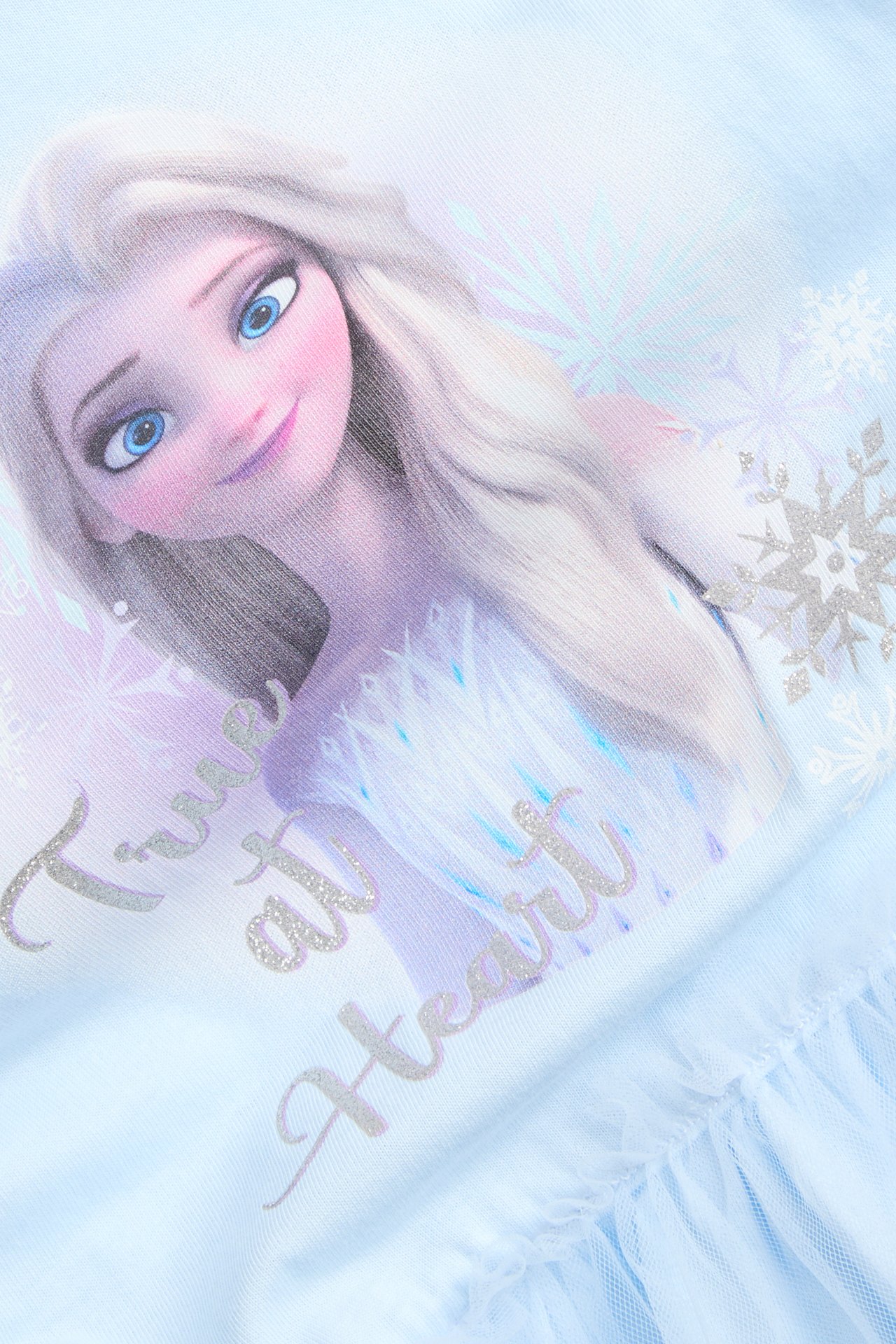Nærbilde: Lys blå barnekjole i jersey med Frost Elsa-trykk, glittertekst og tyllskjørt.