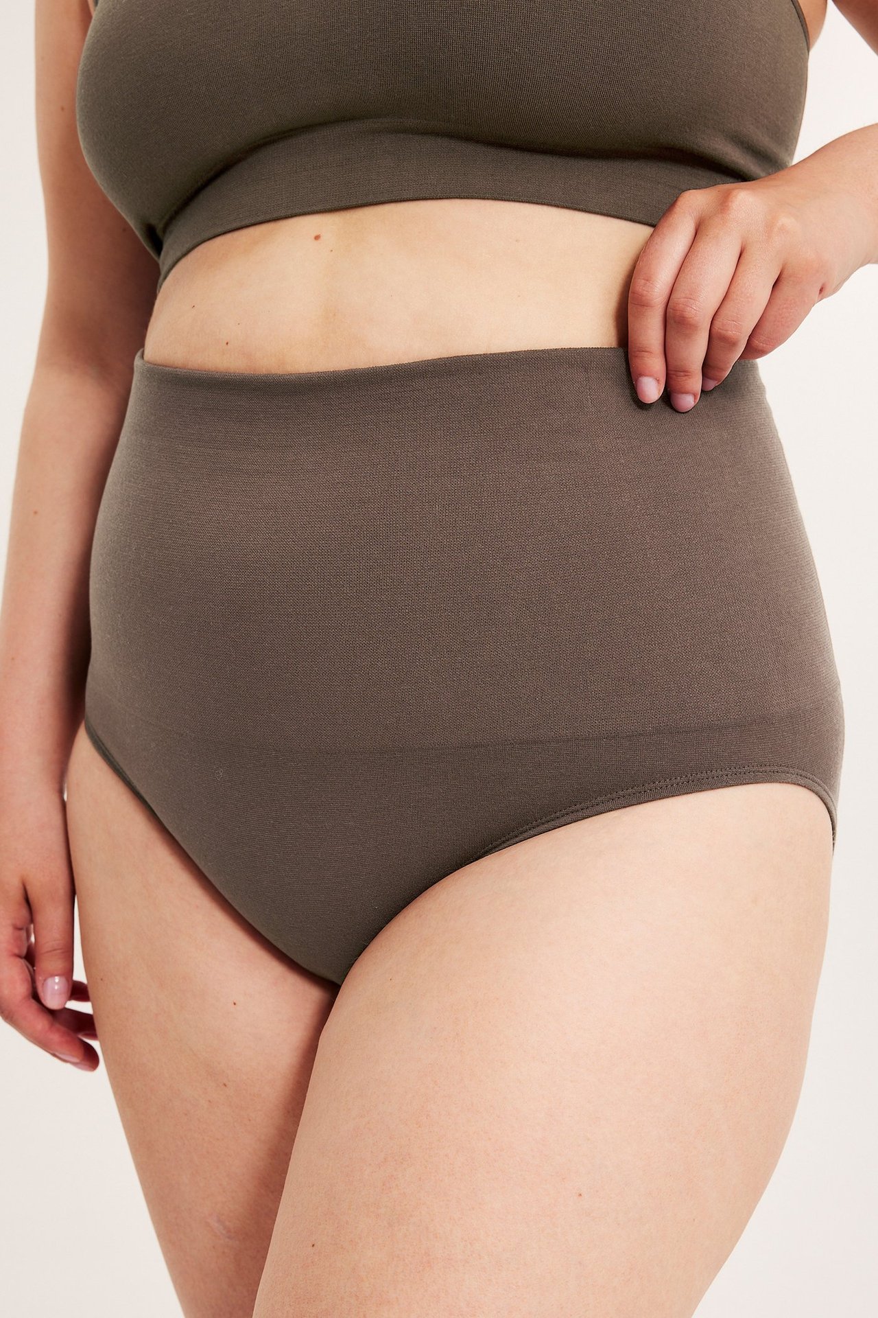 Lähikuva sivukuva naisesta yllään tummanruskeat saumattomat korkeavyötäröiset alushousut ja yhteensopiva rintaliivitoppi.