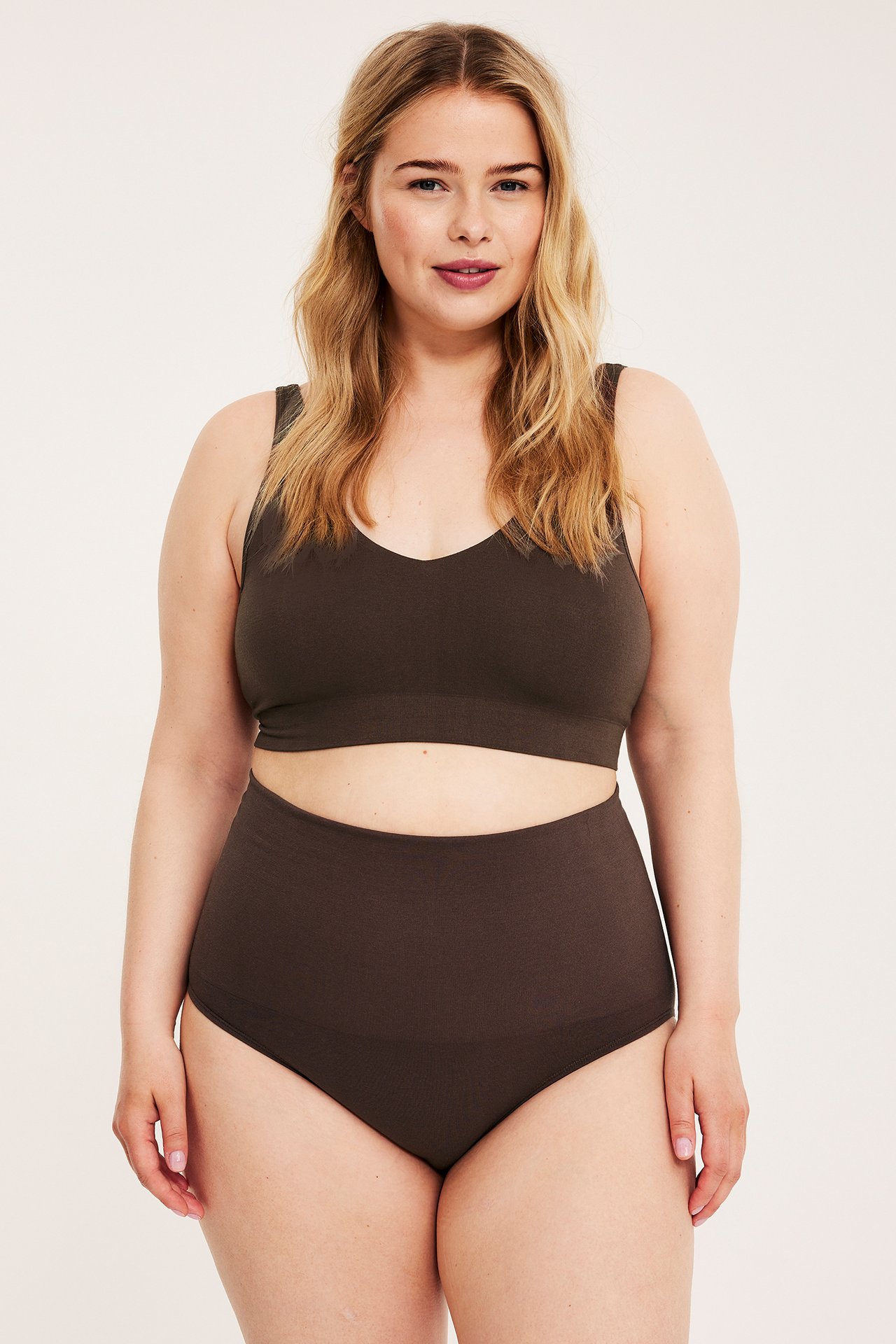 Framifrån kvinna i mörkbrun sömlös trosa med extra hög midja och matchande sömlös BH-topp.