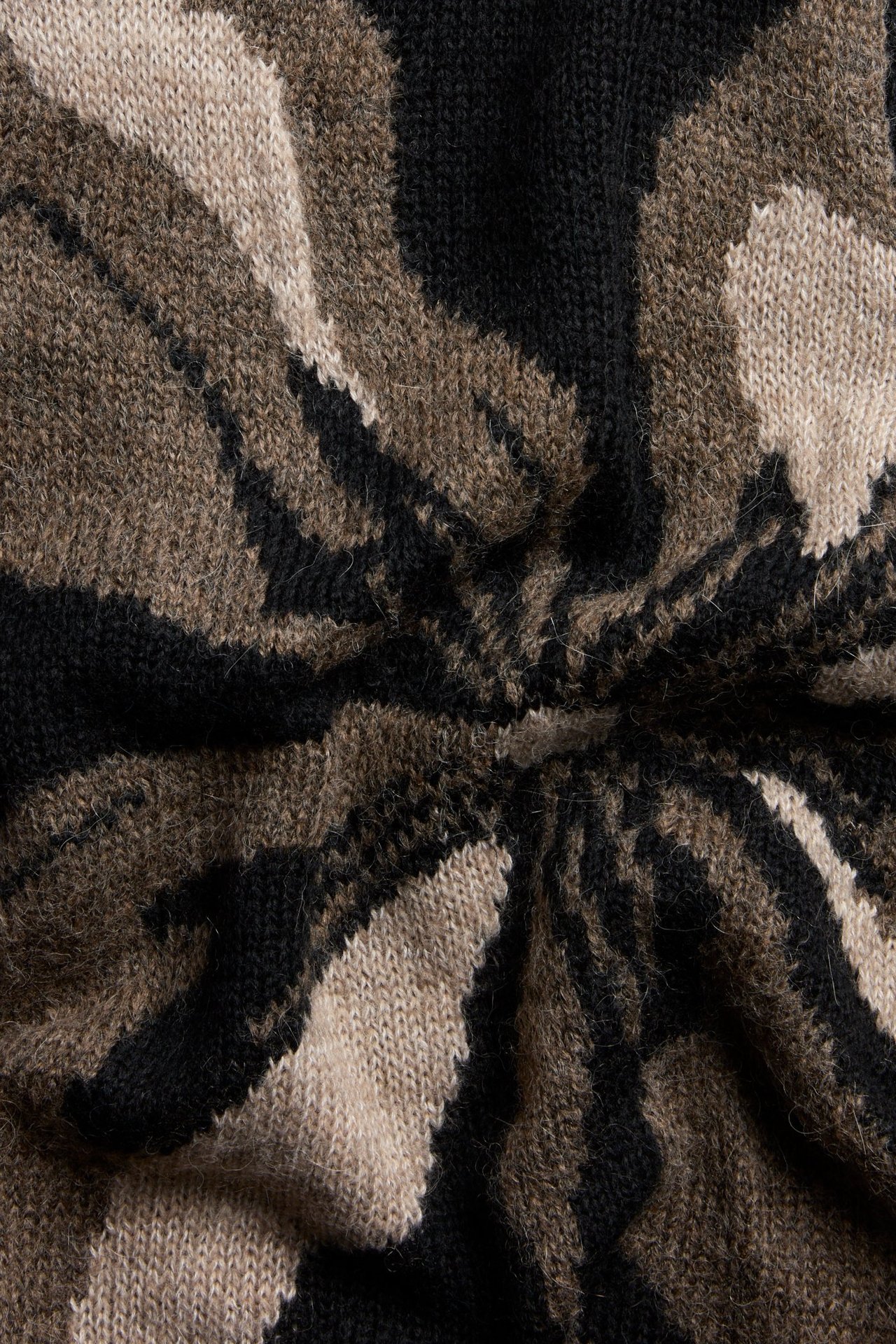 Zbliżenie czarnego, brązowego i beżowego swetra z dzianiny intarsjowej w kwiatowy wzór.