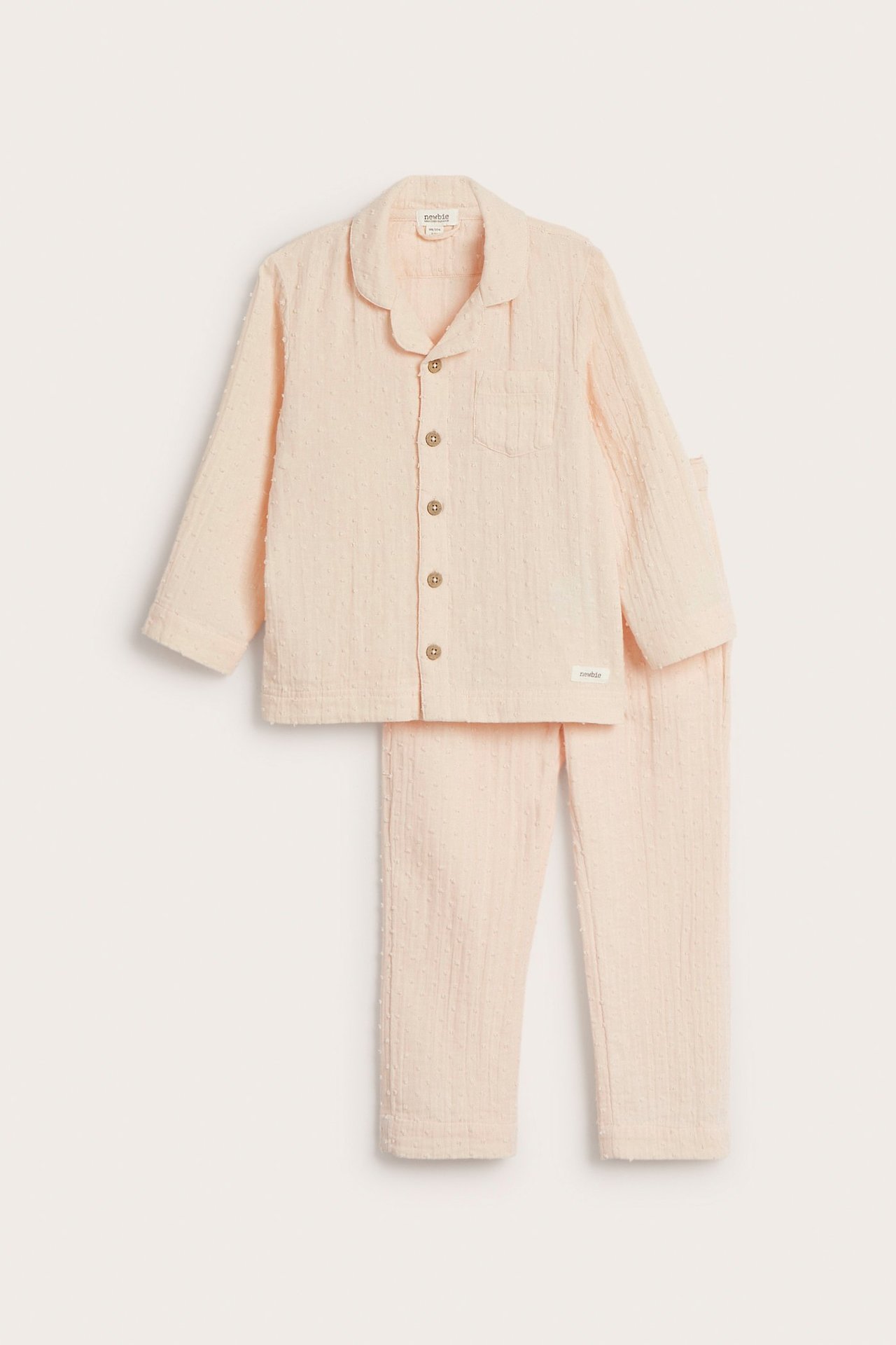 Edestä näkymä lapsen vaaleanoranssista pilkullisesta puuvillapyjamasta, jossa kauluspaita ja yhteensopivat housut.