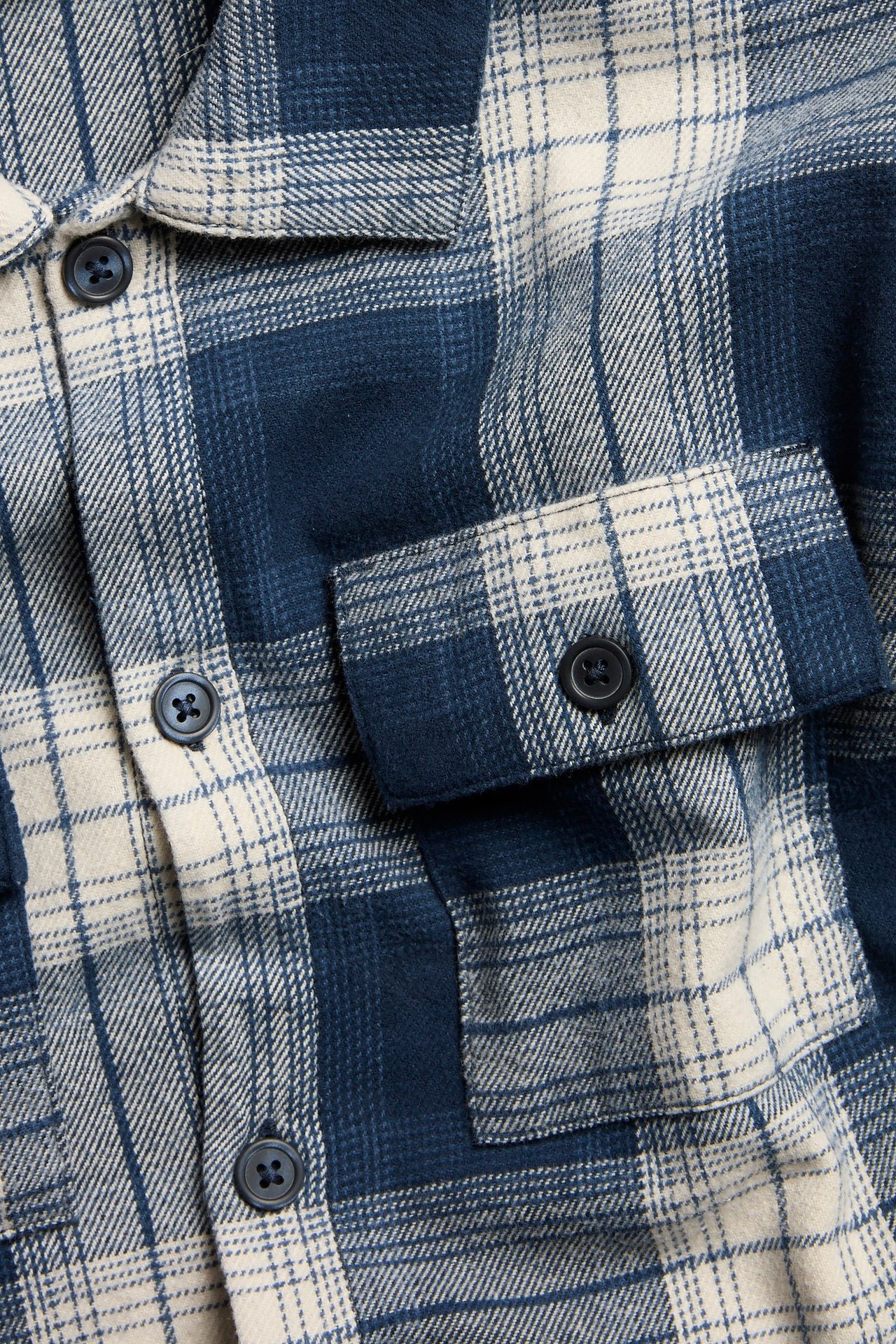 Zbliżenie na granatową i kremową koszulę w kratę z flaneli, z guzikami i kieszenią na piersi.