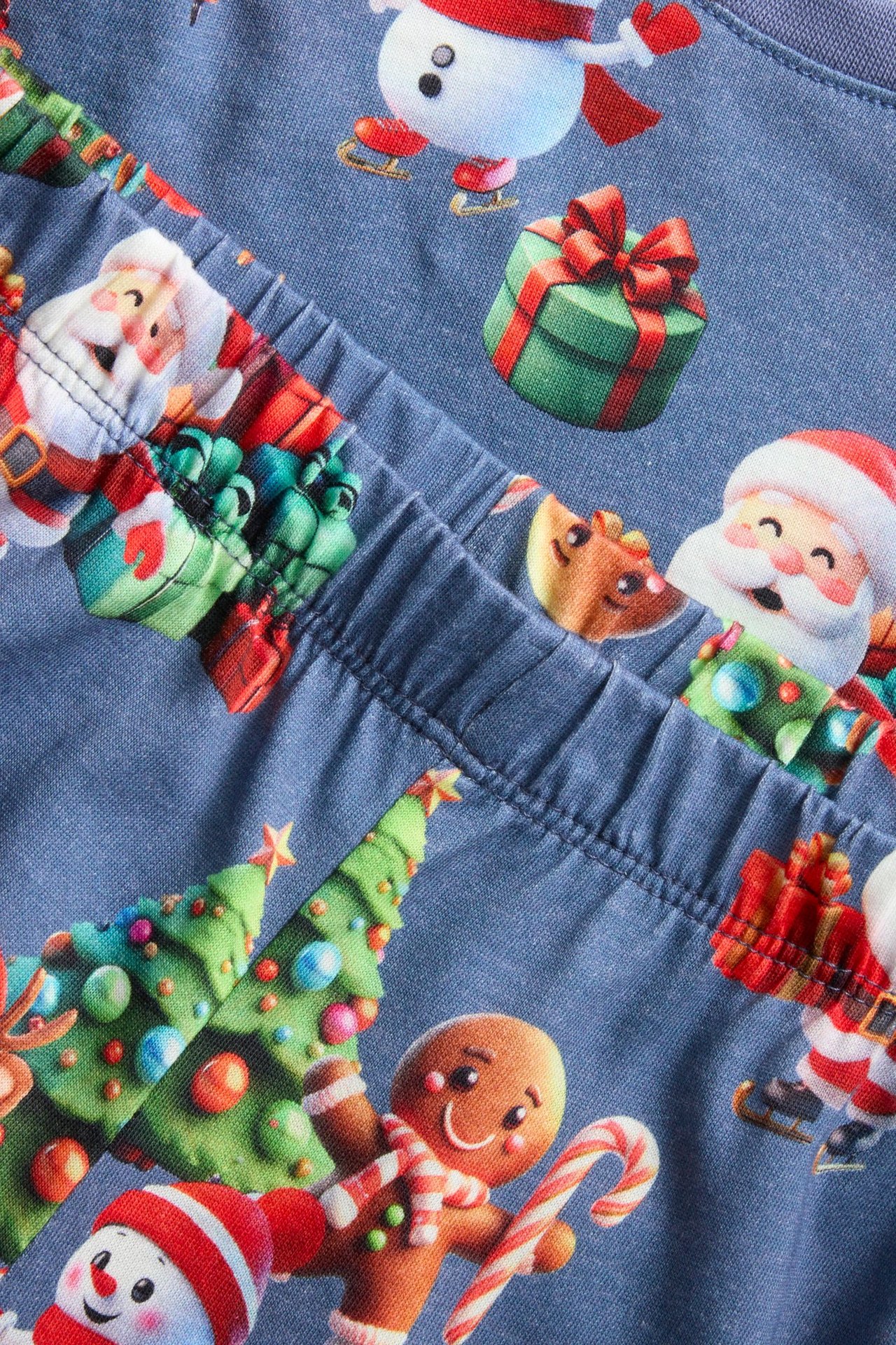 Närbild: blå bomullsjulpyjamas för barn med jultema mönster och resår i midjan.
