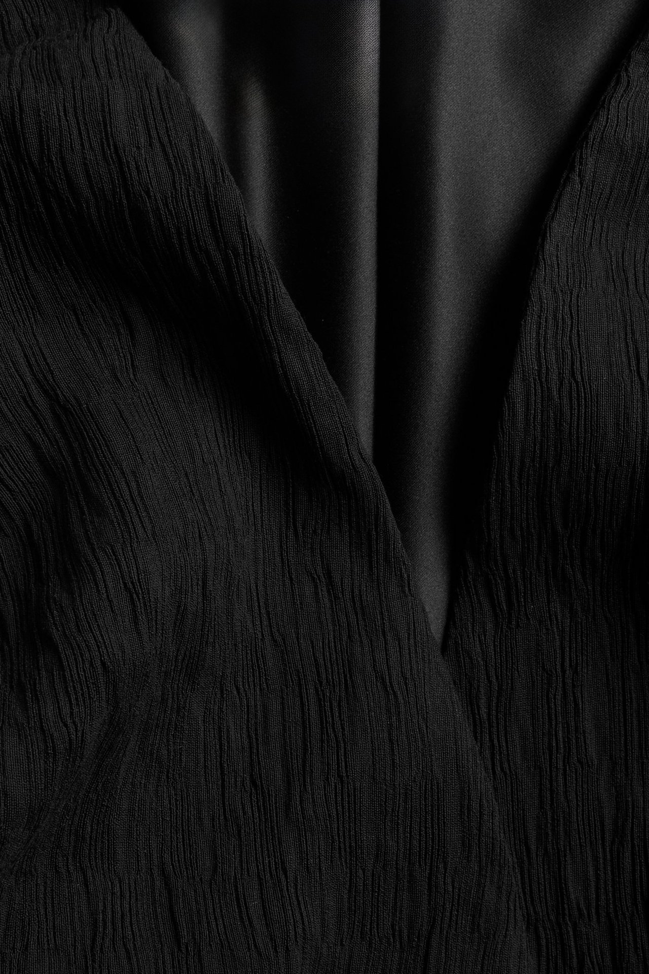 Zbliżenie czarnej marynarki z teksturowanym materiałem zewnętrznym i gładką czarną podszewką.