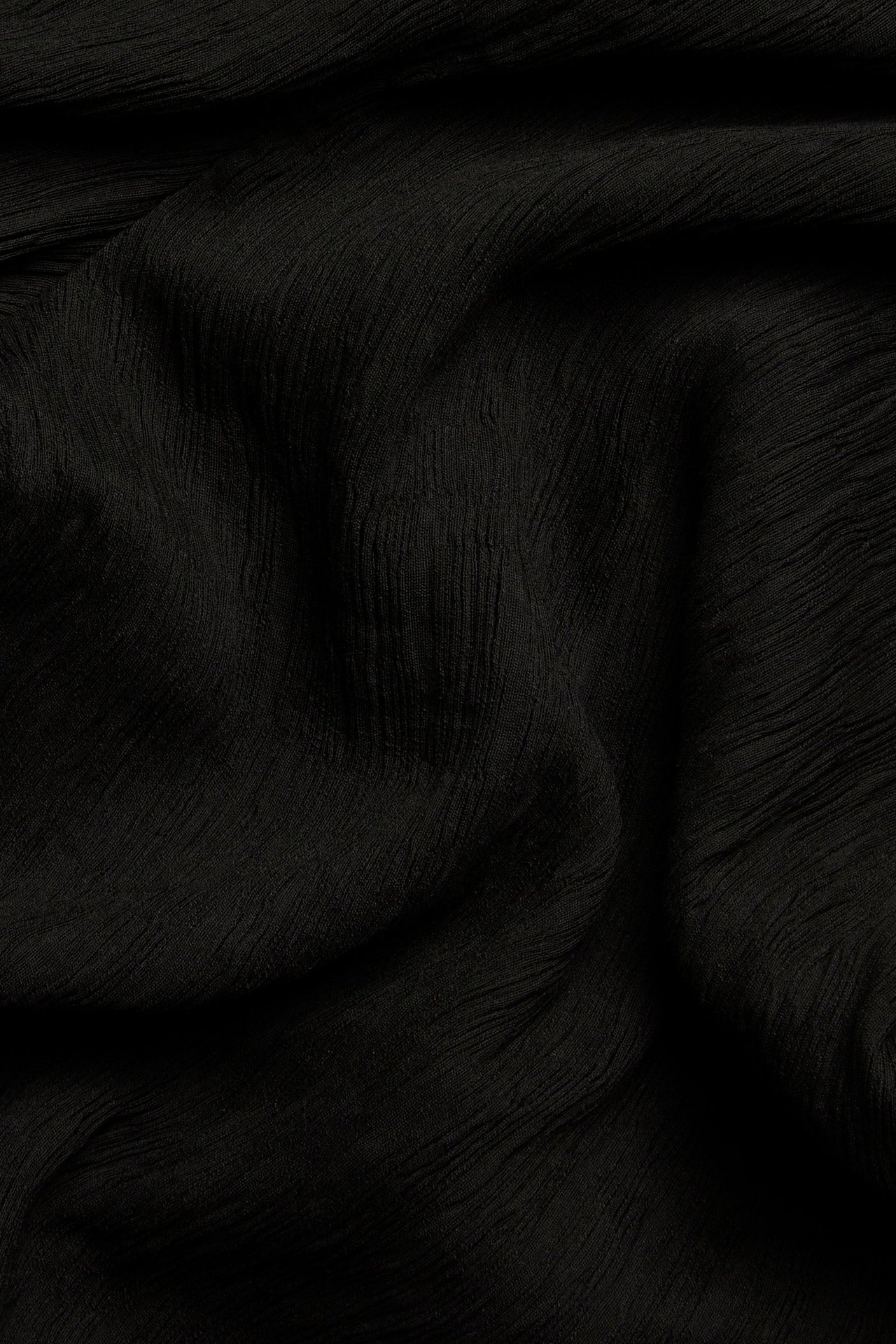 Zbliżenie czarnego, jednolitego materiału o subtelnej, pogniecionej fakturze.