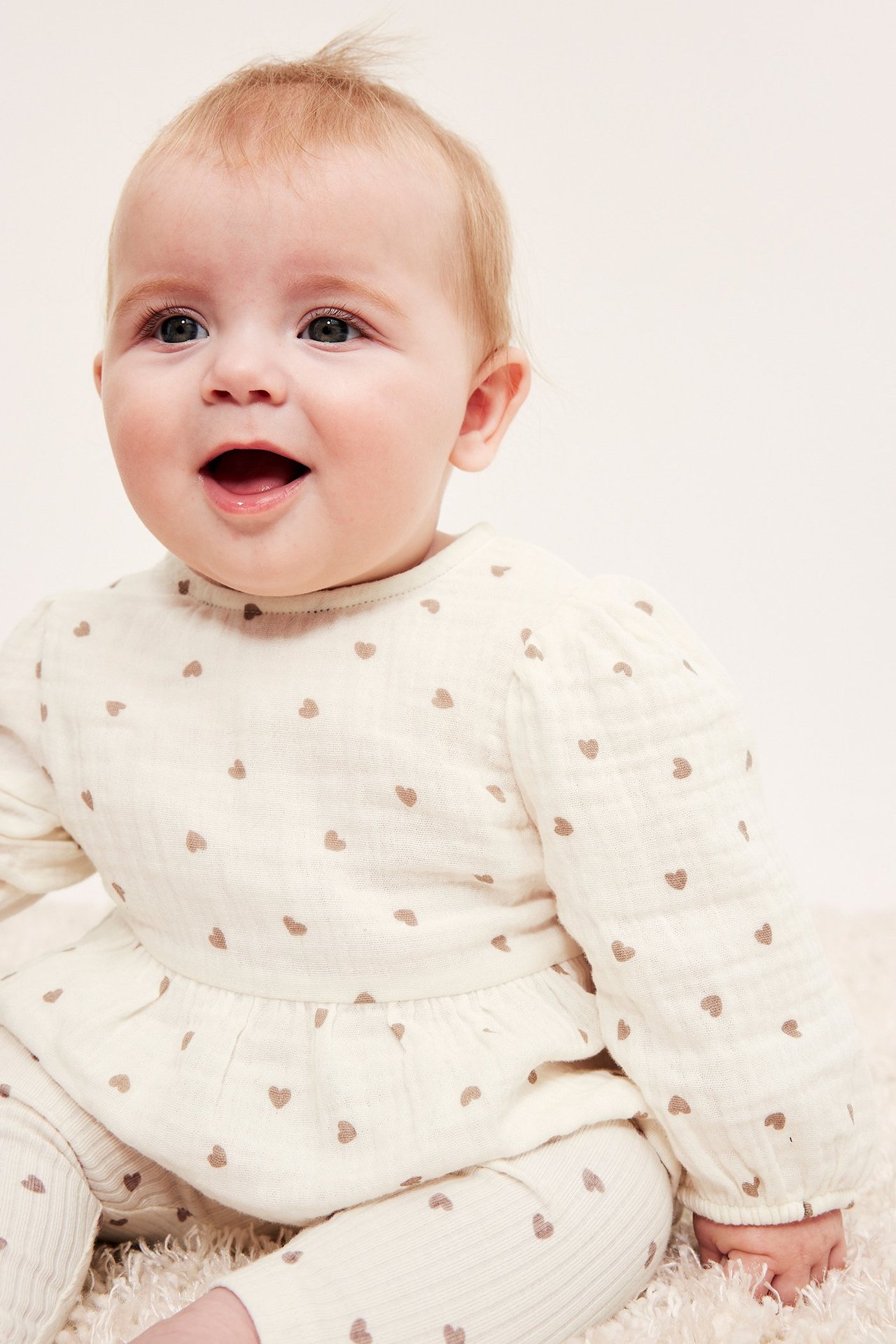 Widok z przodu: niemowlę w ecru bluzce peplum z muślinu w brązowe serca i pasujących prążkowanych legginsach.
