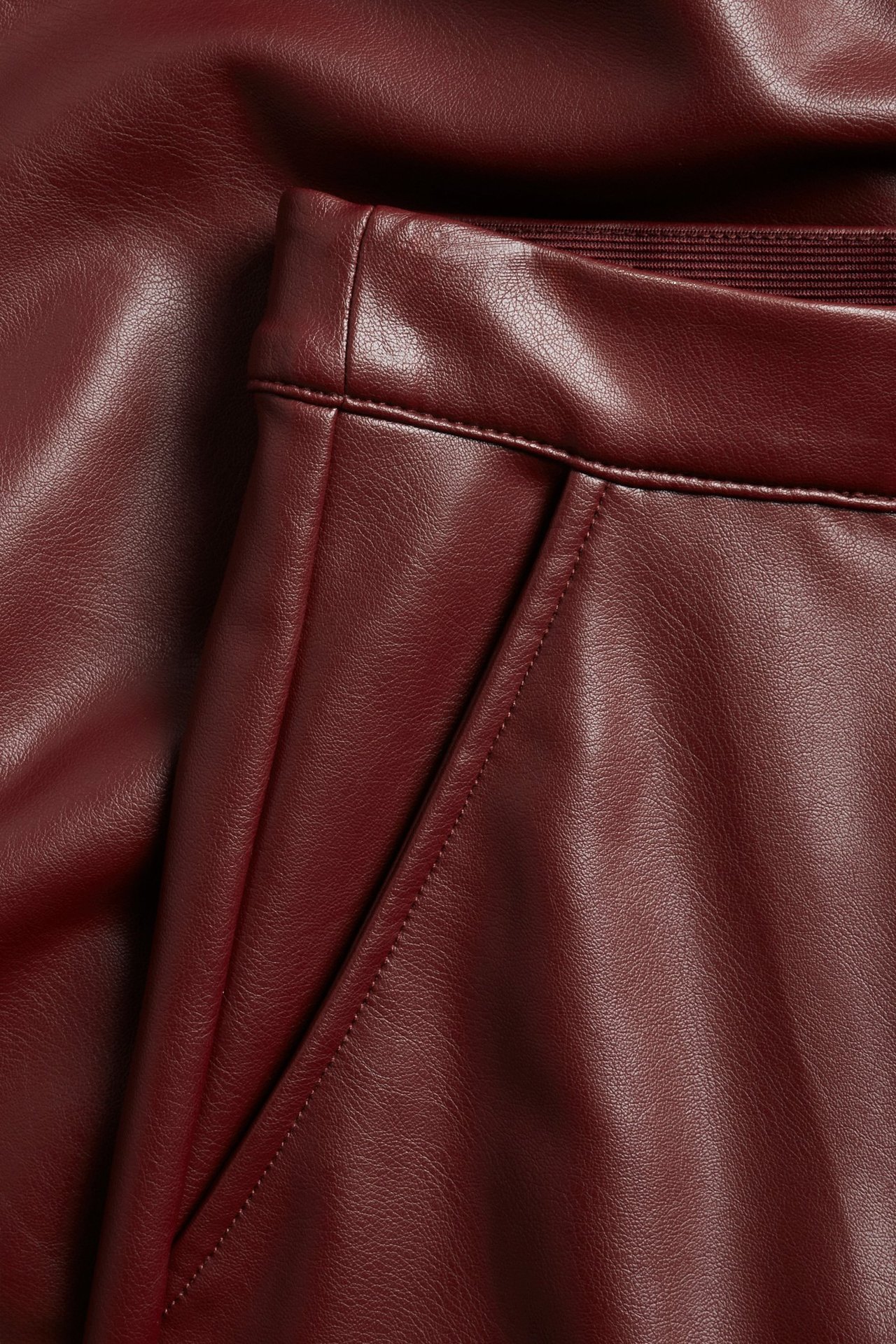 Zbliżenie czerwonej spódnicy ze sztucznej skóry z kieszenią i elastycznym pasem.