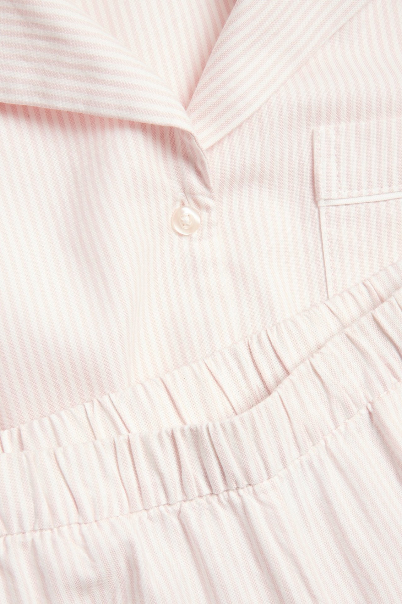 Zbliżenie różowej, pasiasto-białej, bawełnianej piżamy z zapinaną koszulą i elastyczną talią spodni.