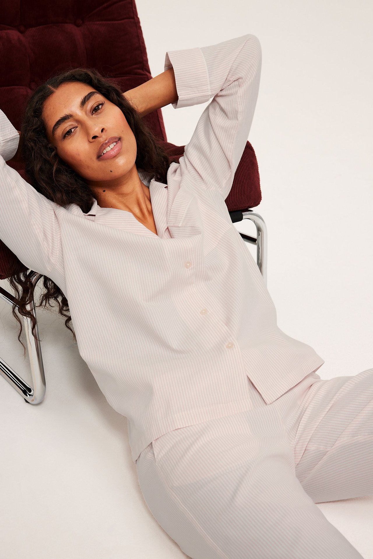 Kobieta w różowo-pasiastych piżamach, leżąca na krześle, kieszenie, guziki, przeszycia.