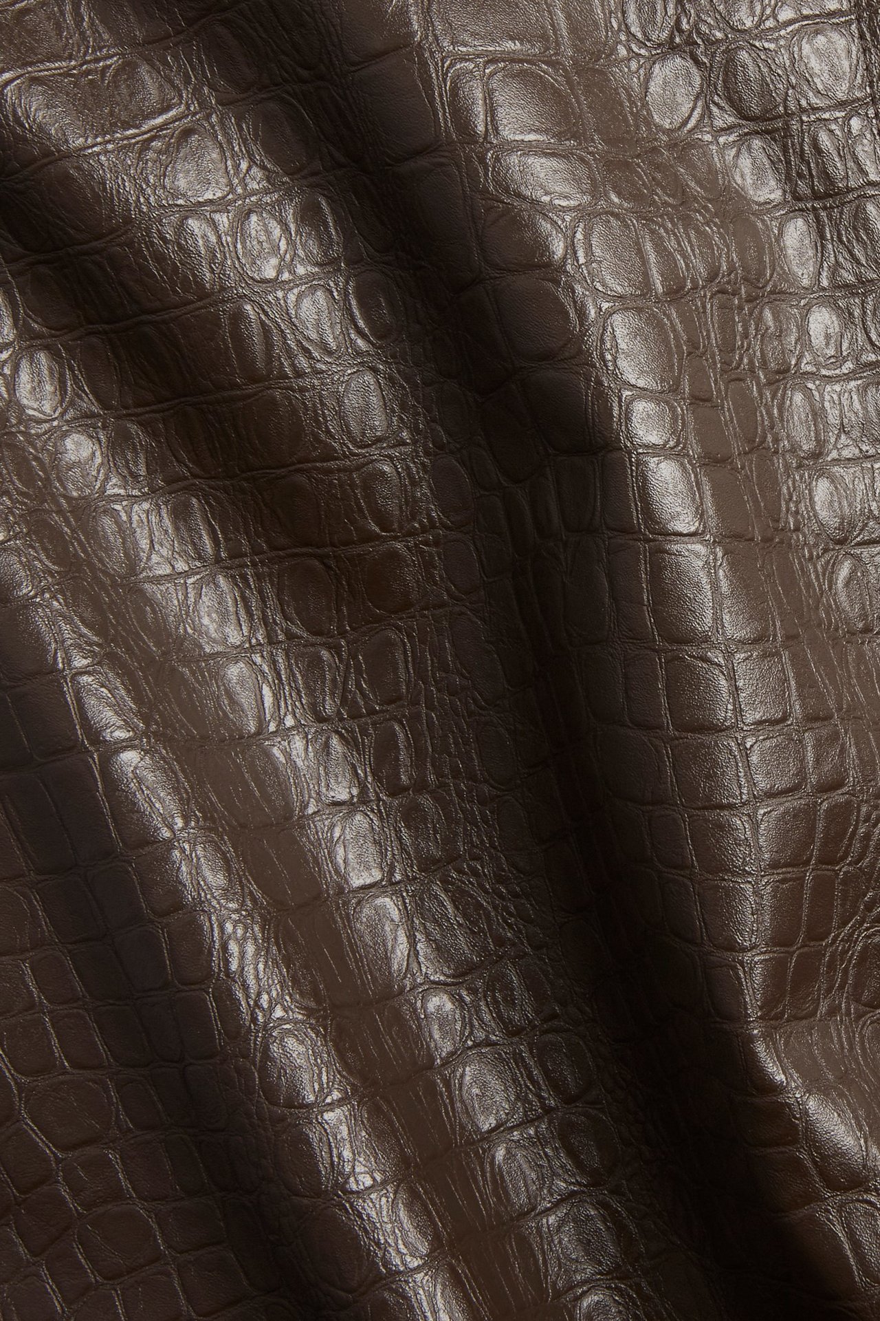 Zbliżenie na ciemnobrązową spódnicę z imitacji skóry o strukturalnym wzorze krokodyla.