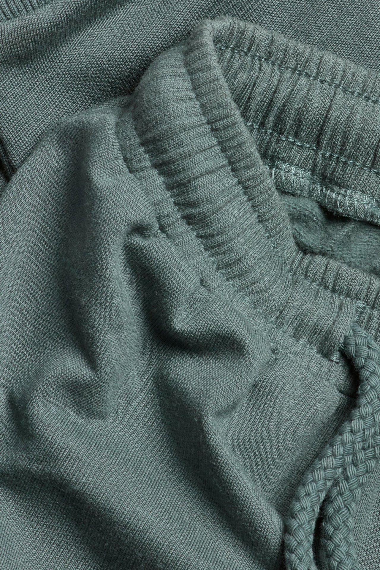 Lähikuva khakinvihreistä puuvillasekoitteisista collegehousuista, joissa on joustava kiristysnyörivyötärö.