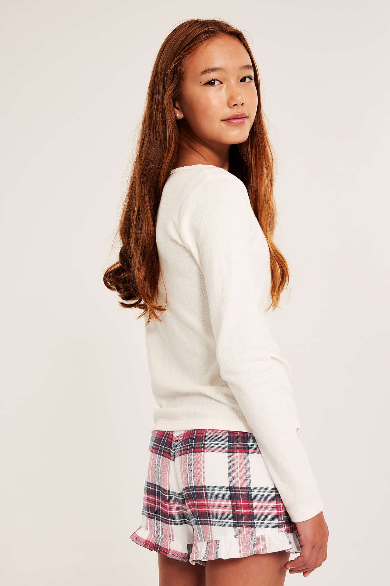 Sidebilde av barn i røde, hvitrutete flanellshorts med rysjer og en kremfarget langermet topp.