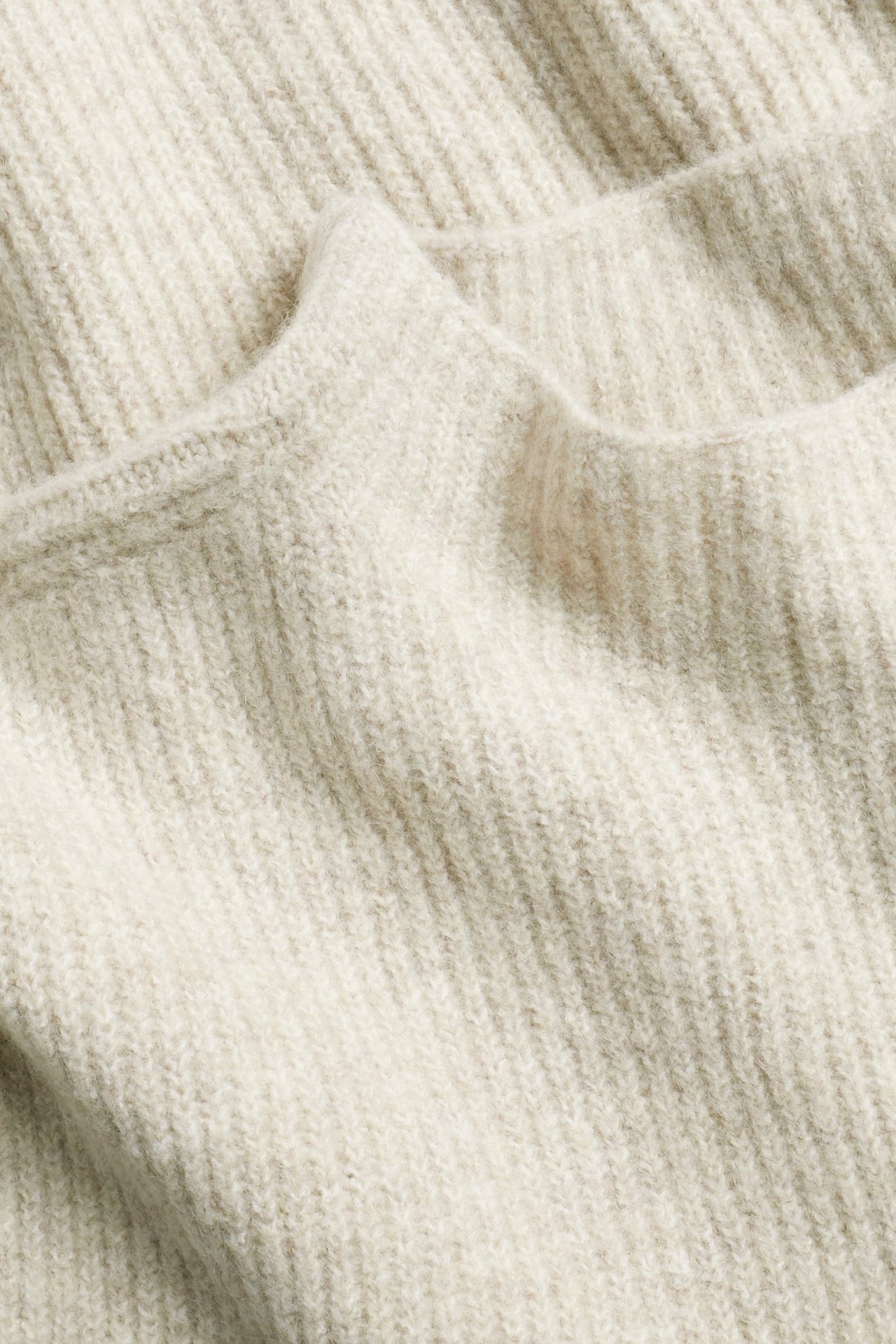 Zbliżenie beżowej melanżowej dzianiny prążkowanej kamizelki, ukazujące jej wzorzystą fakturę.