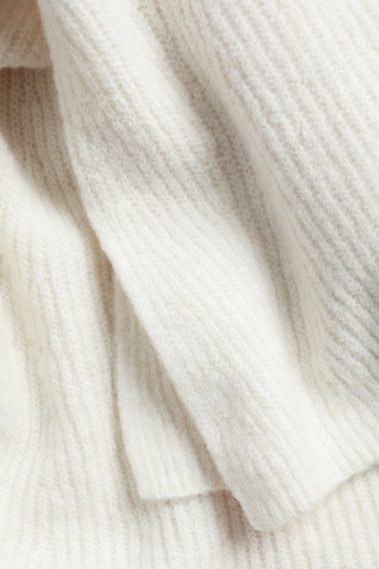 Zbliżenie jasnobeżowego swetra w prążki o strukturalnym wzorze.