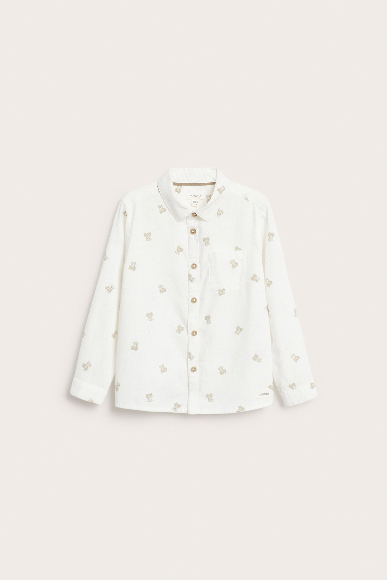 Framsida av en offwhite bomullsskjorta i twill för barn med bruna björnmönster och knappar fram.